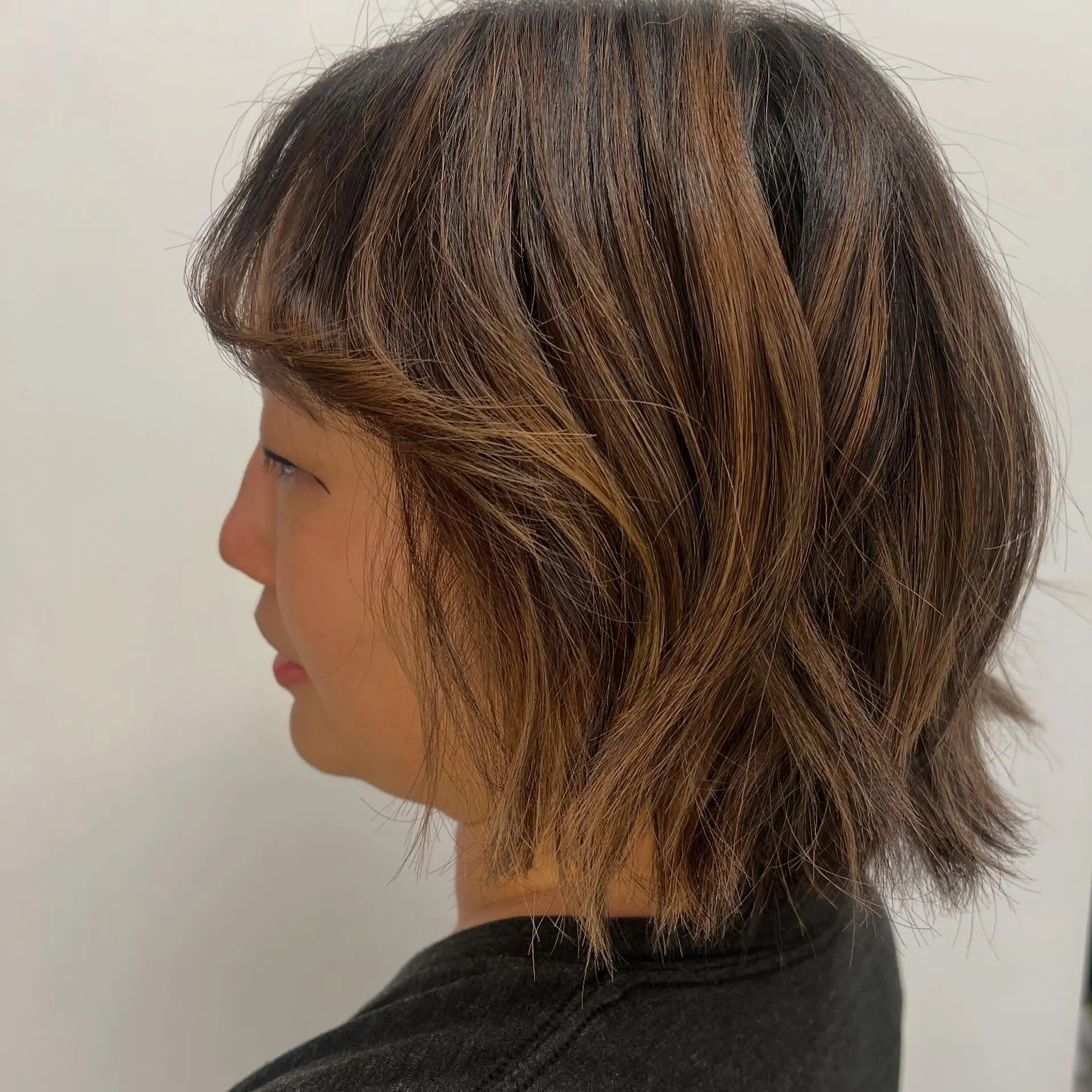 A textured short bob haircut featuring soft layers, a wispy fringe, and warm dimensional highlights. 1