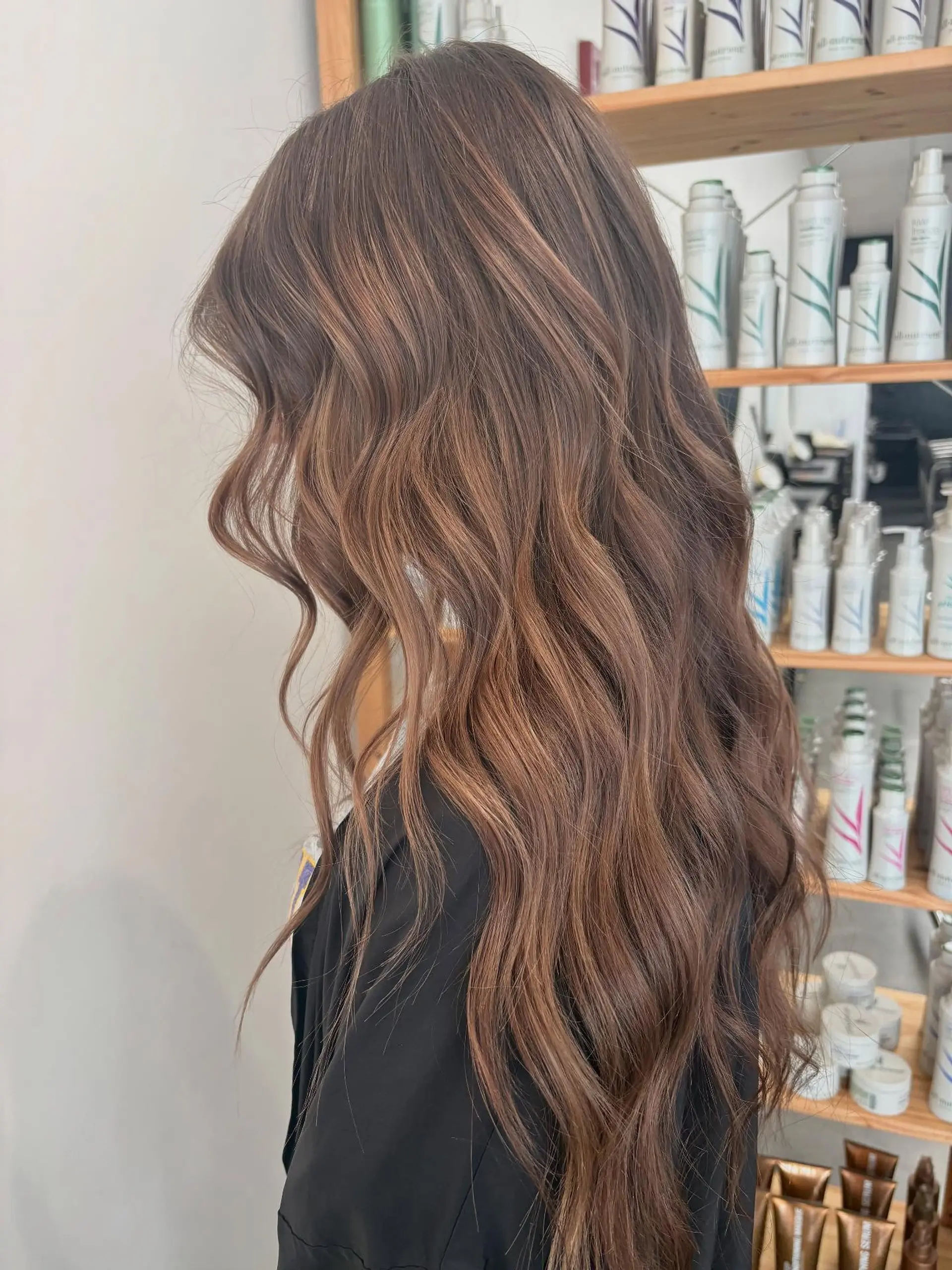 Long, warm-toned brunette hair styled in soft, cascading waves with subtle dimensional ribbons of lighter brown. 1