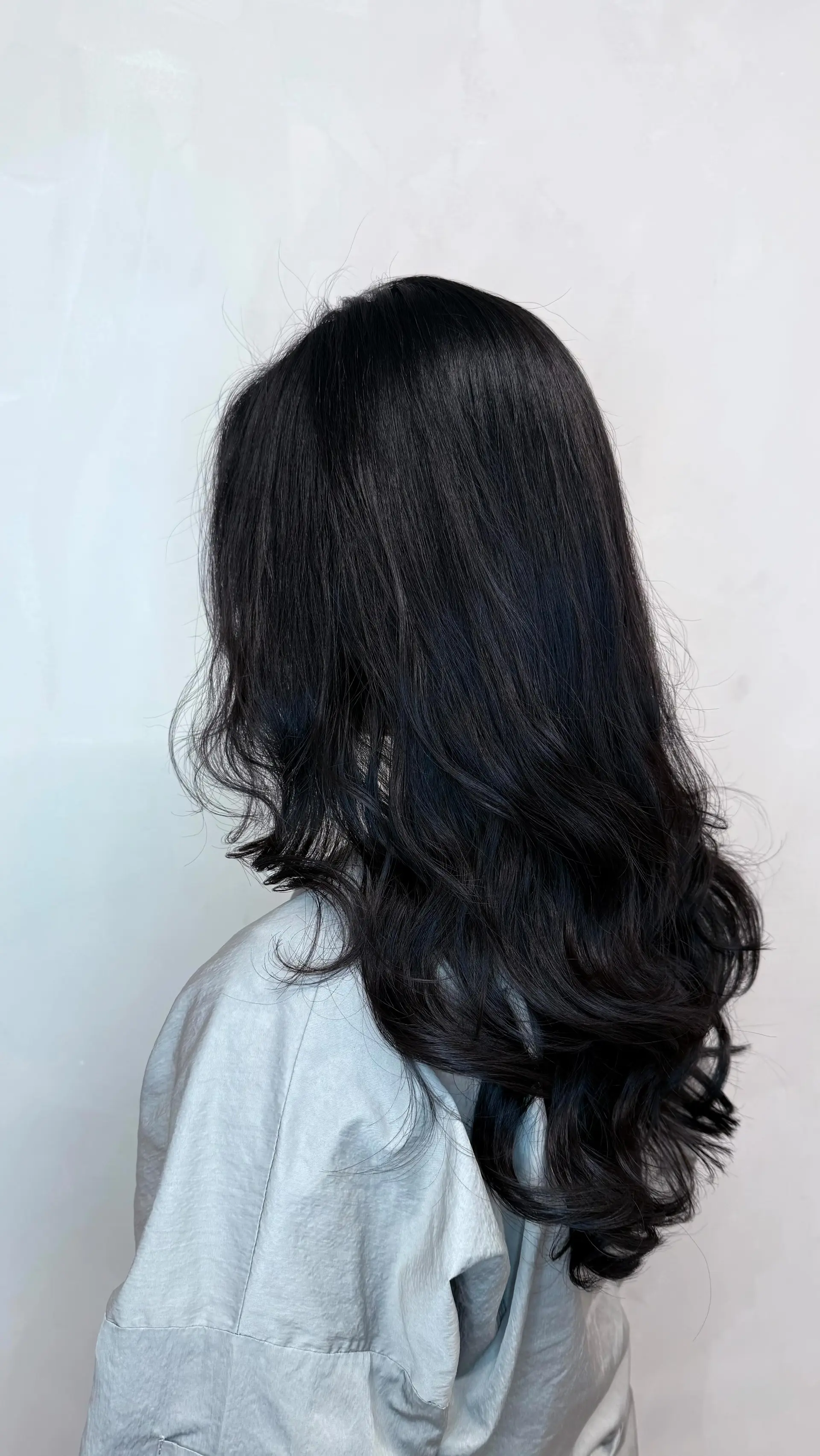 Long layered jet black hair styled with soft, voluminous waves throughout the ends. 1