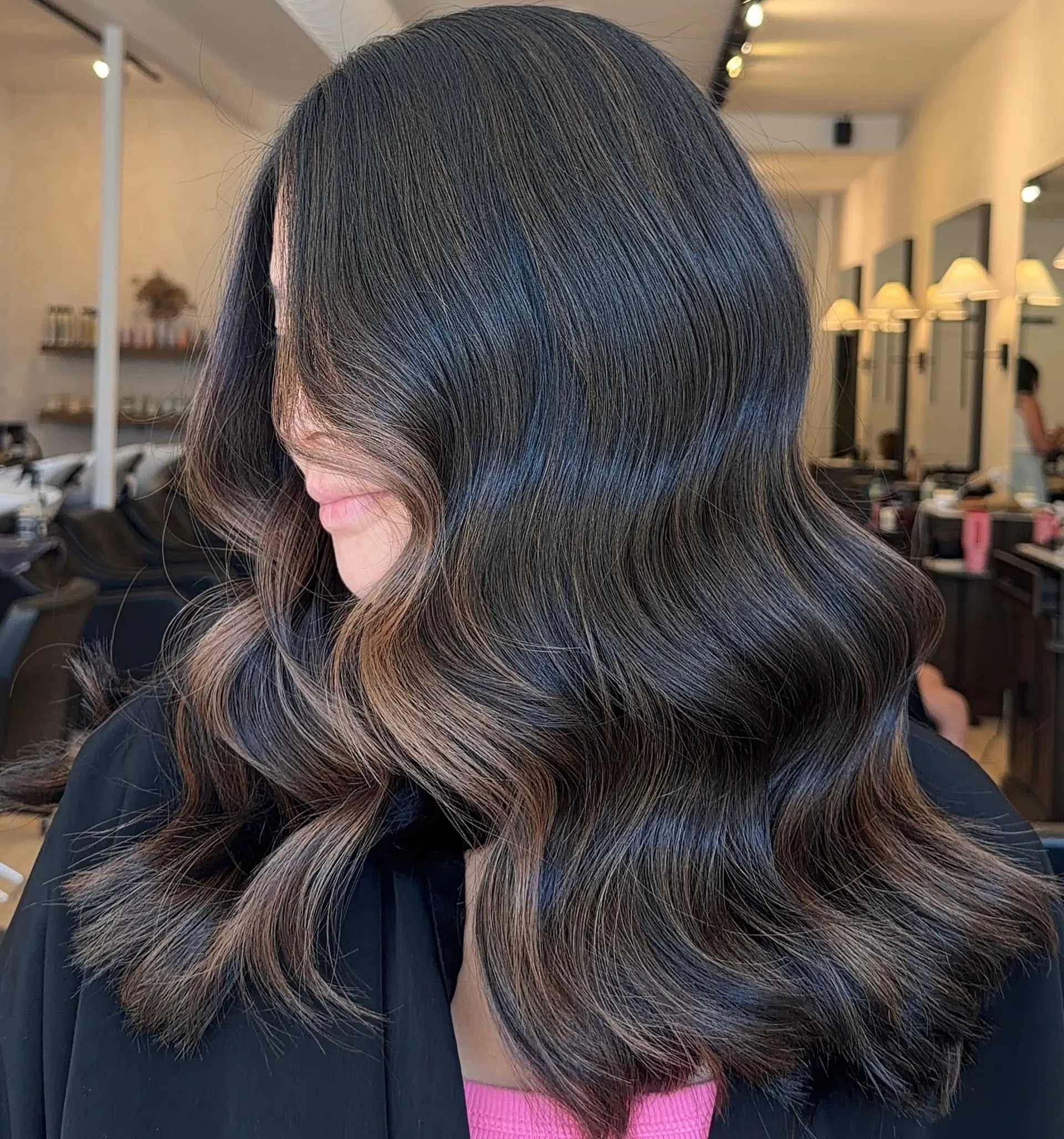Glossy dark brunette hair styled into smooth, sculpted waves with warm caramel dimensional highlights throughout. 1