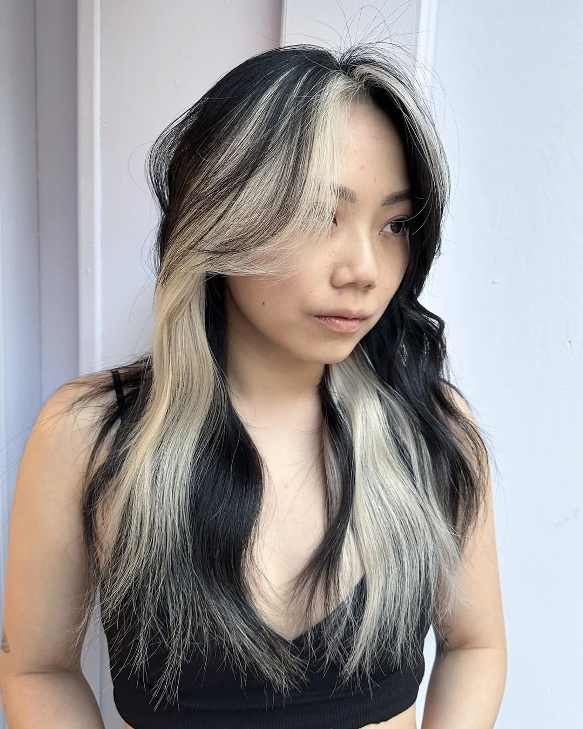 This hairstyle features wavy, long hair with a striking combination of jet-black and platinum blonde colors. It has a center part with face-framing layers and dramatic contrasting highlights. 1
