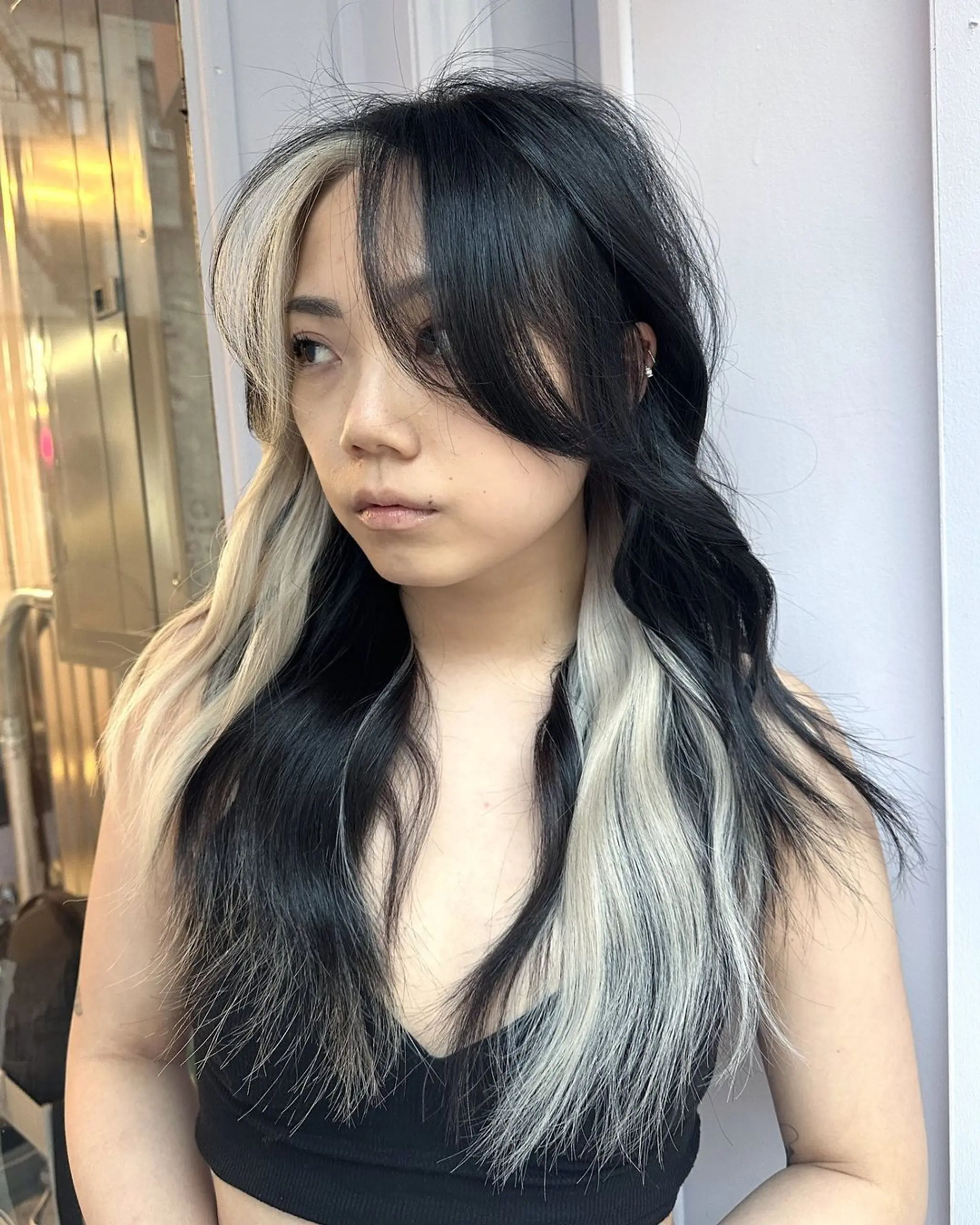 This hairstyle features wavy, long hair with a striking combination of jet-black and platinum blonde colors. It has a center part with face-framing layers and dramatic contrasting highlights. 2