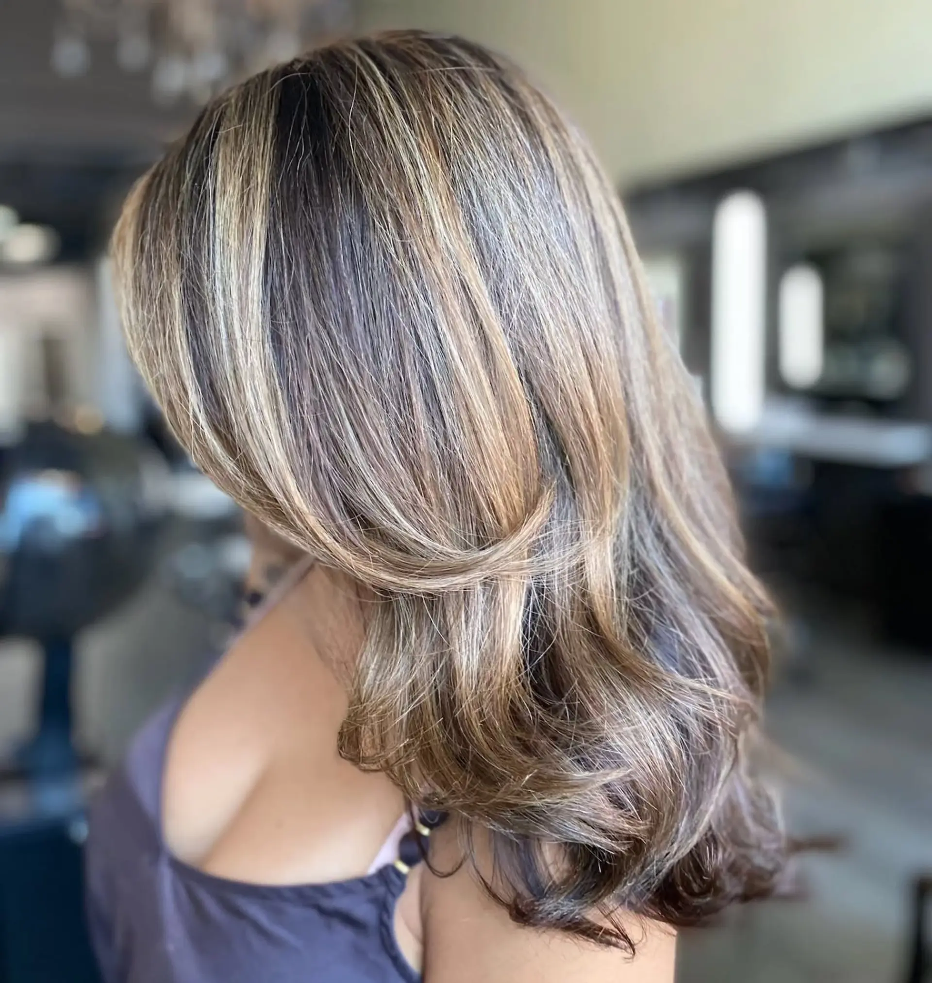 Long layered hair featuring ribbon-like dimensional blonde highlights over a light brown base, styled with a polished, voluminous blowout and soft curved ends. 1