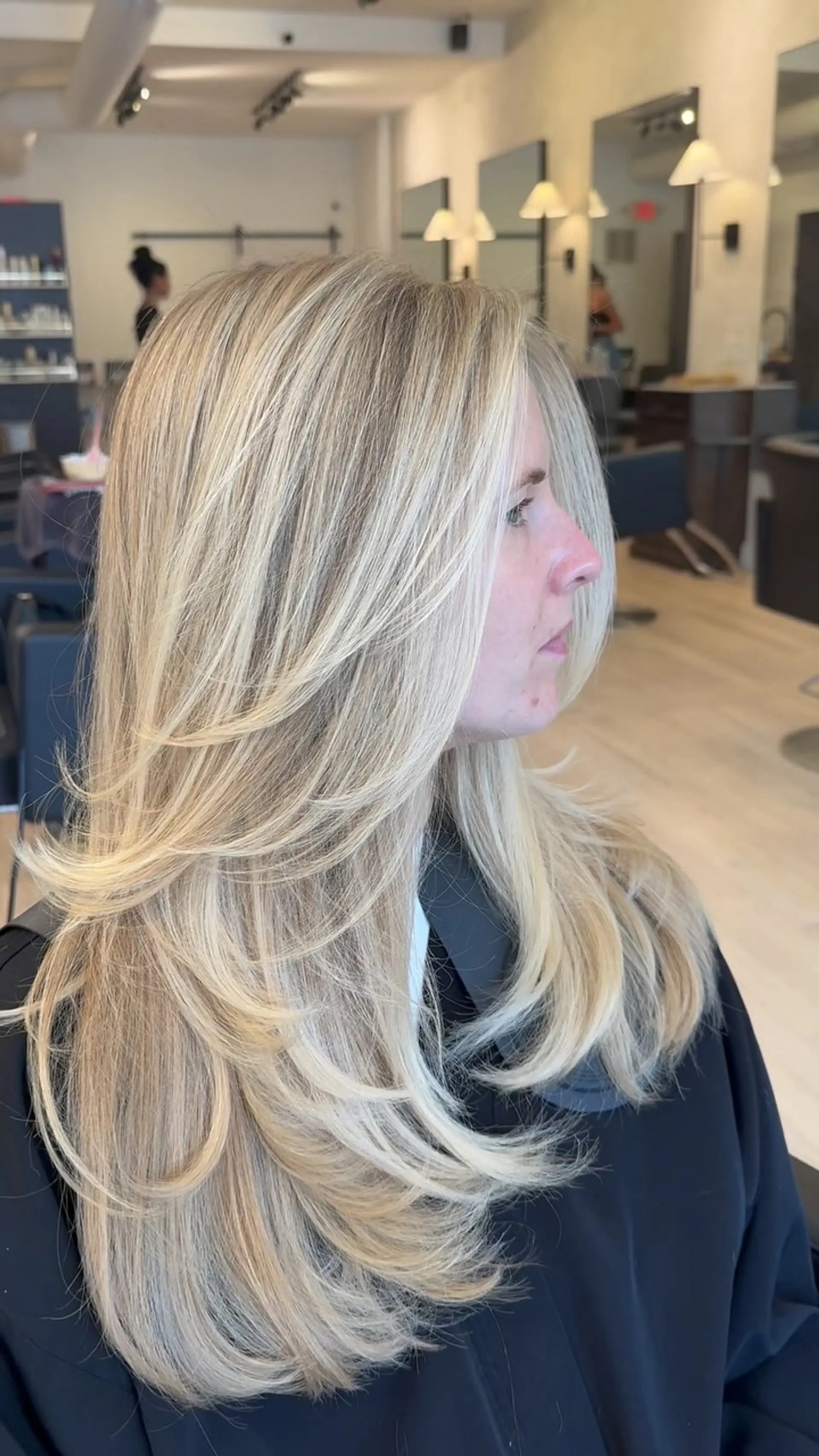 Long bright blonde hair cut into voluminous butterfly layers with a soft blowout. 1