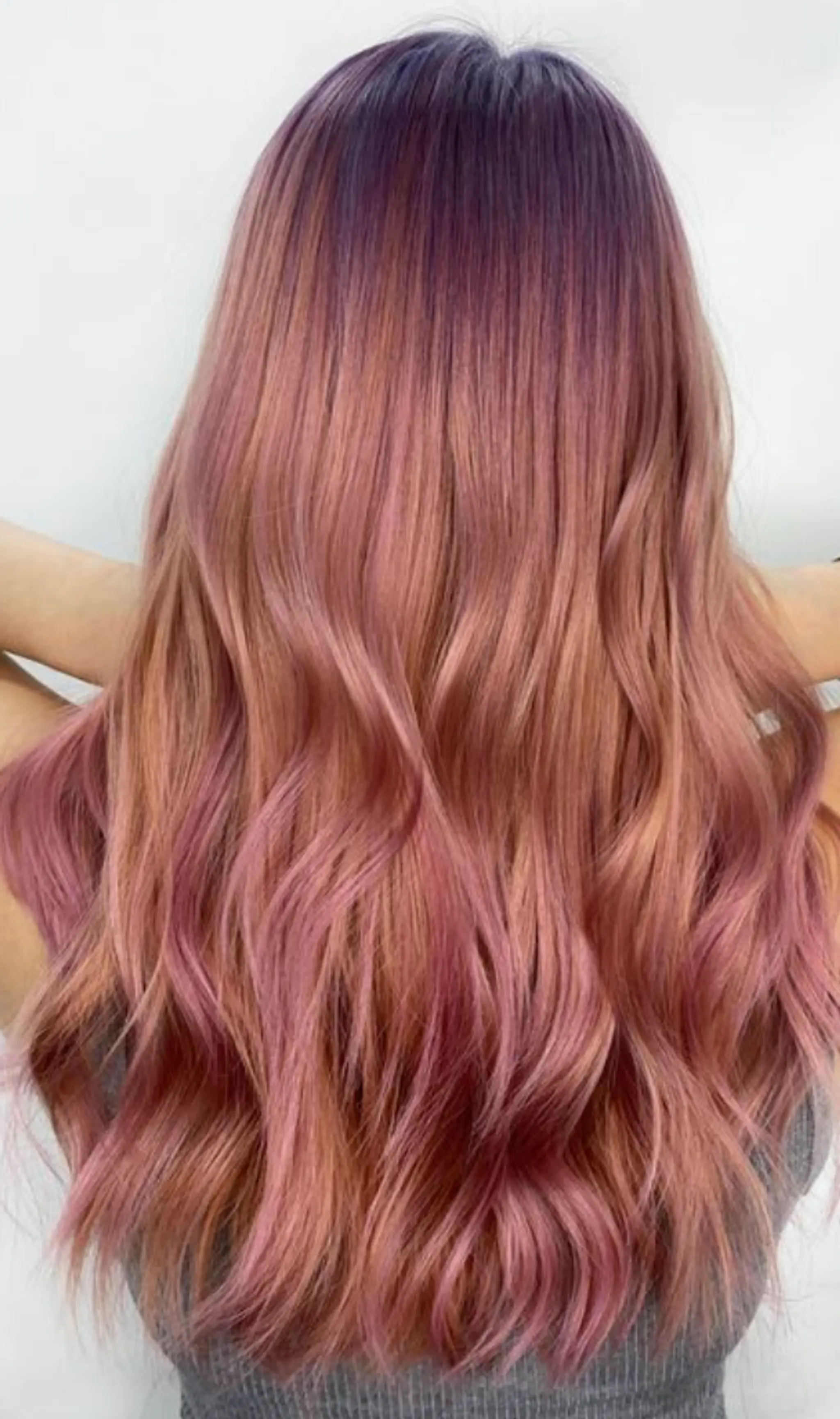 Long, wavy hair cascading in an ombre effect from deep purple at the roots to rose gold and pink at the tips, with loose and voluminous waves.