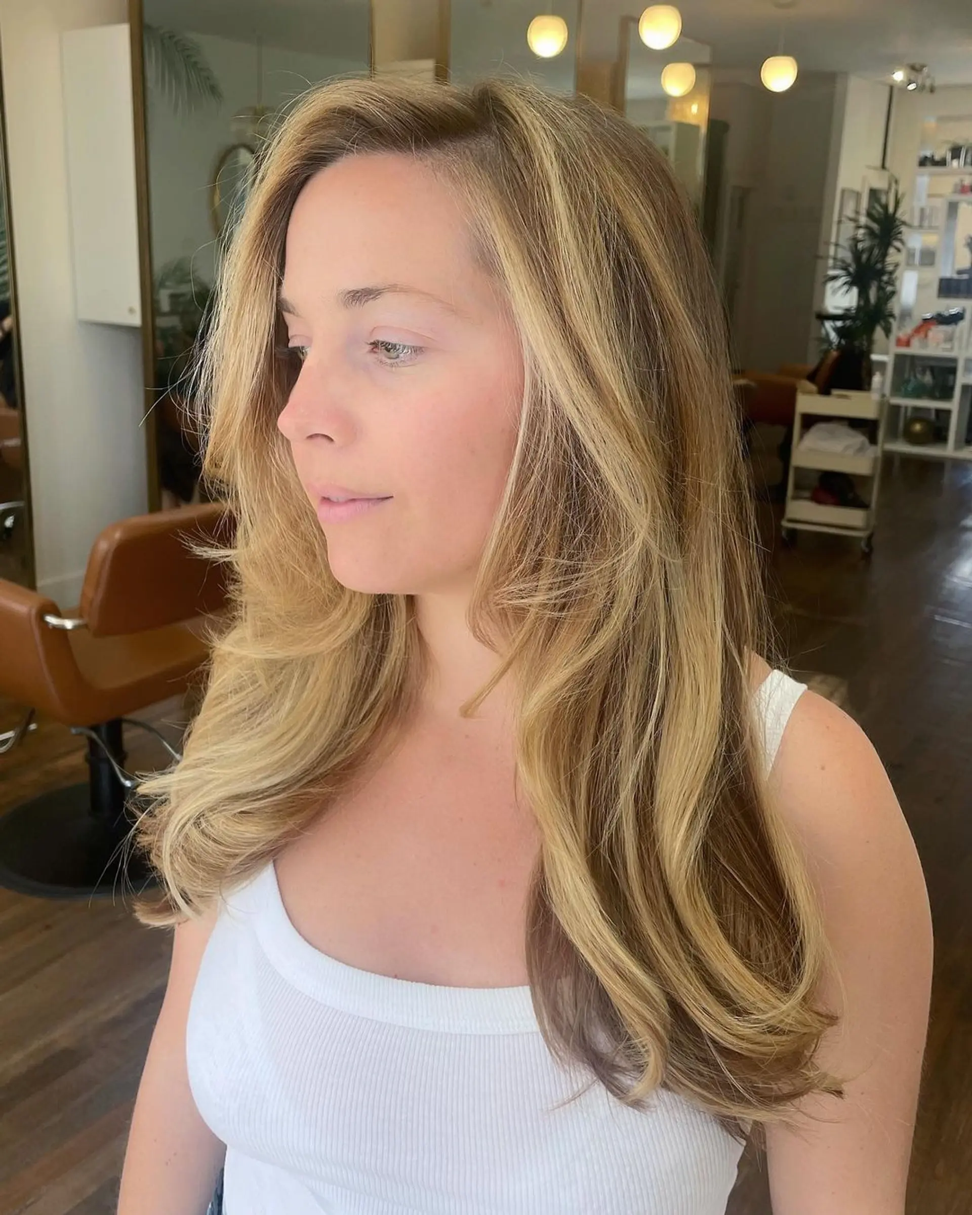 A voluminous long wavy blonde hairstyle with golden highlights. It features layered waves and a side-swept look for added movement and chicness. 2