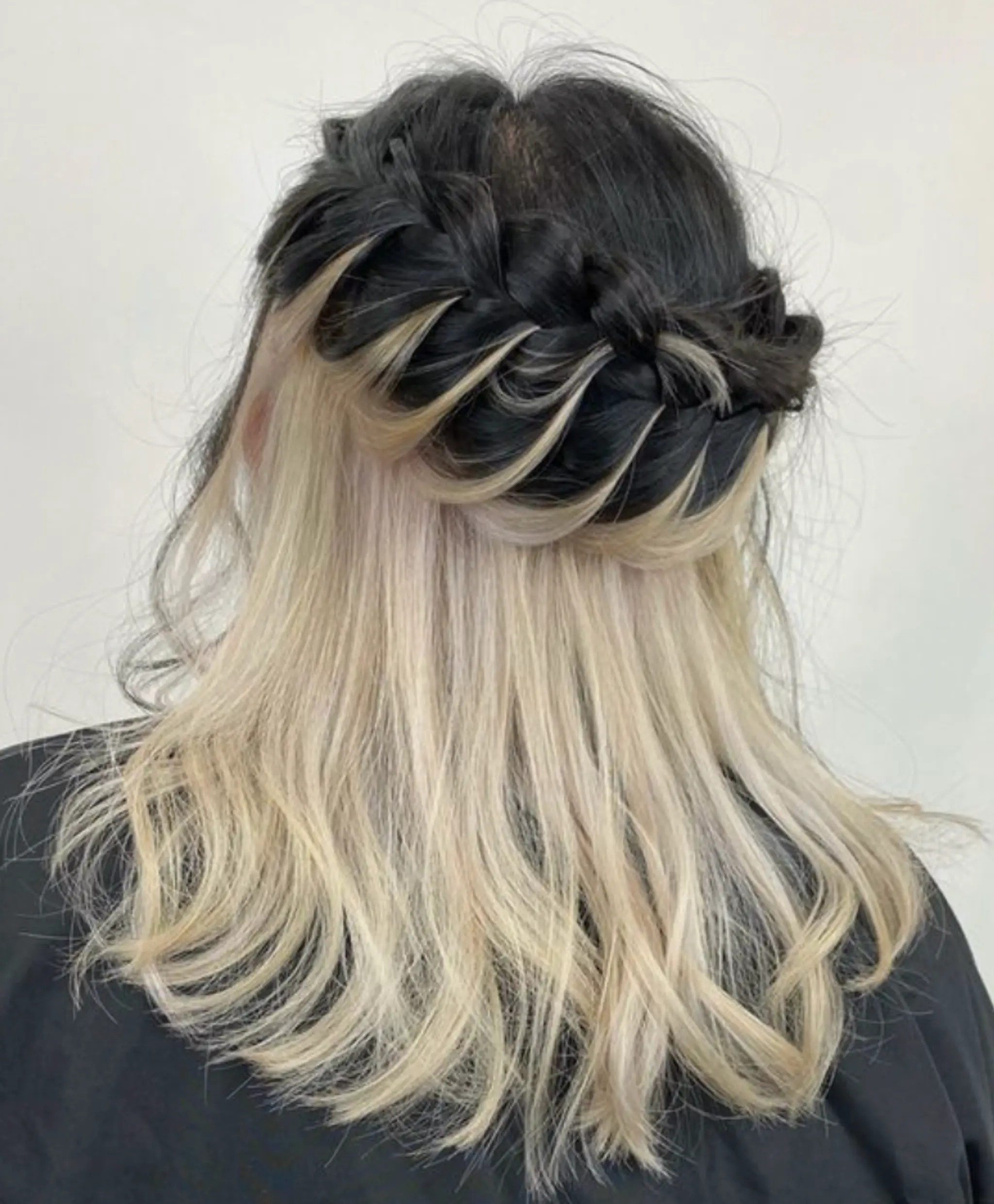 A 'Twist Crown' with a thick, intricate braid wrapping around the crown composed of naturally black hair, contrasted against platinum blonde wavy locks on medium-length hair.