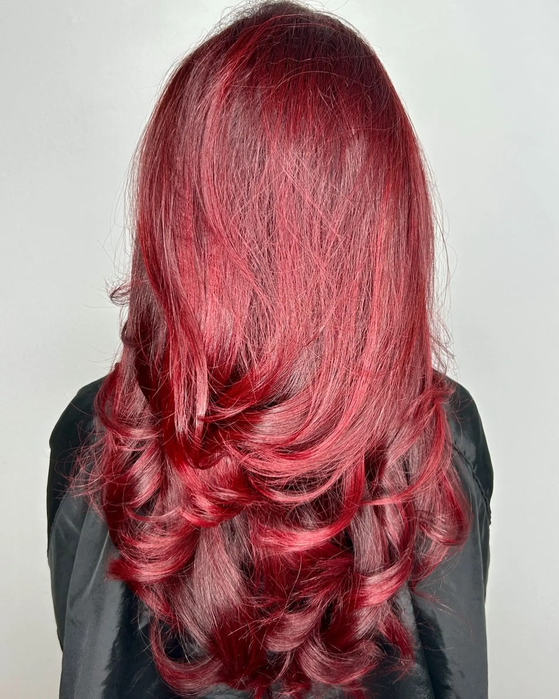Long vivid red hair cut with cascading layers and styled into smooth, voluminous curls at the ends. 1