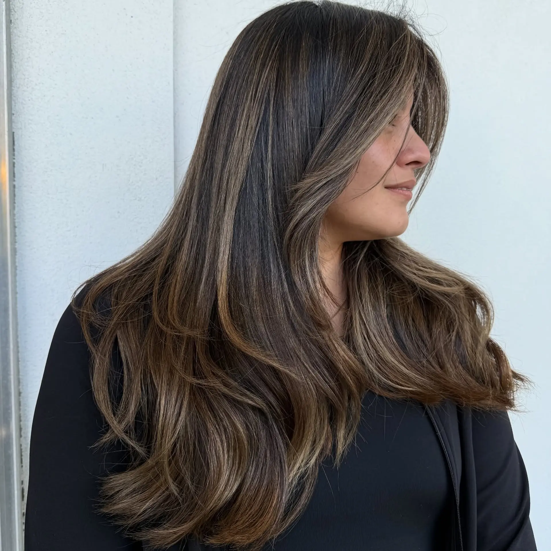 Long layered dark hair enhanced with seamless beige and caramel balayage highlights, styled with soft, flowing waves. 1