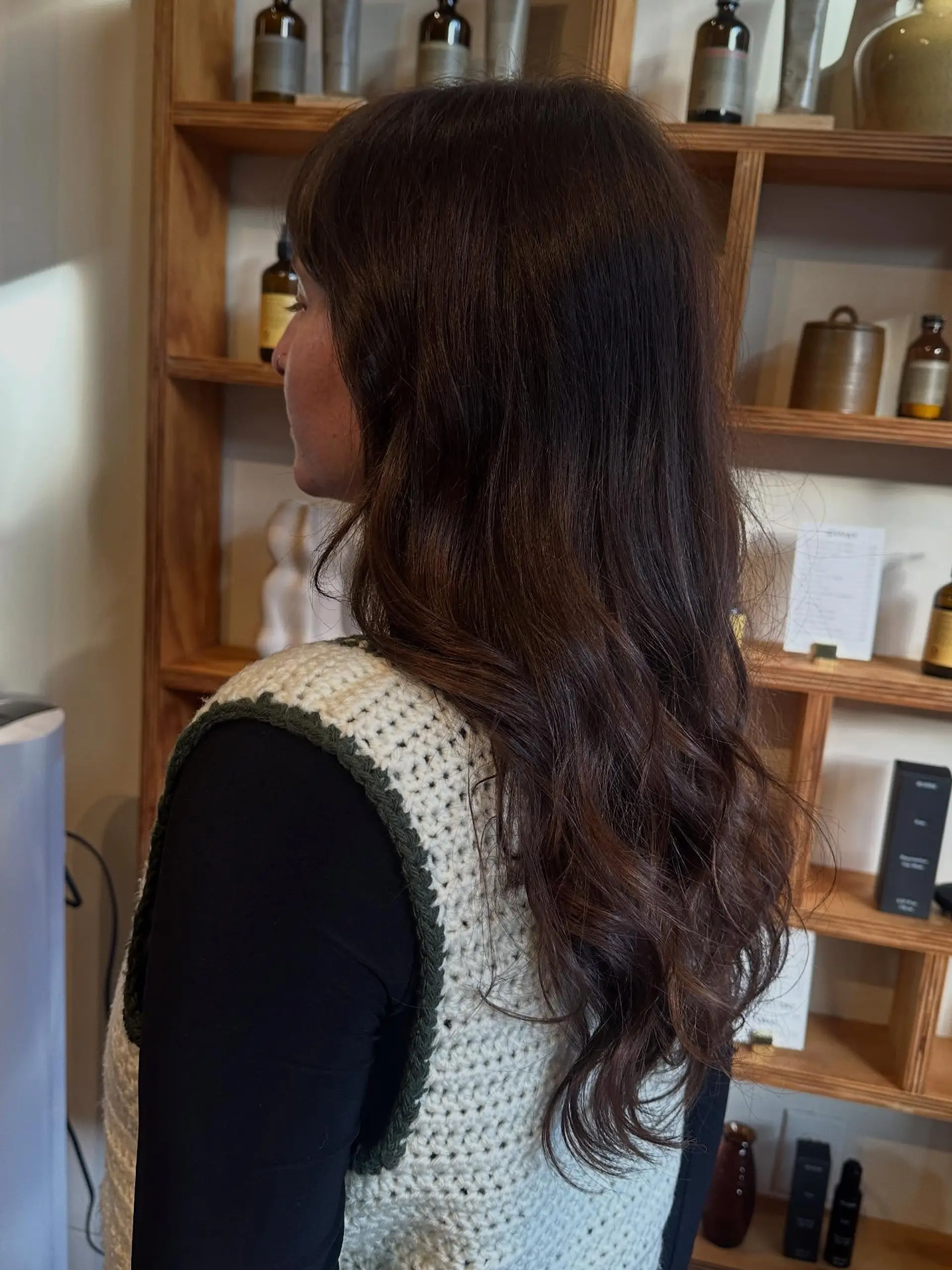 Long dark brunette hair styled with loose waves, subtle hand-painted balayage highlights, and soft fringe bangs. 1