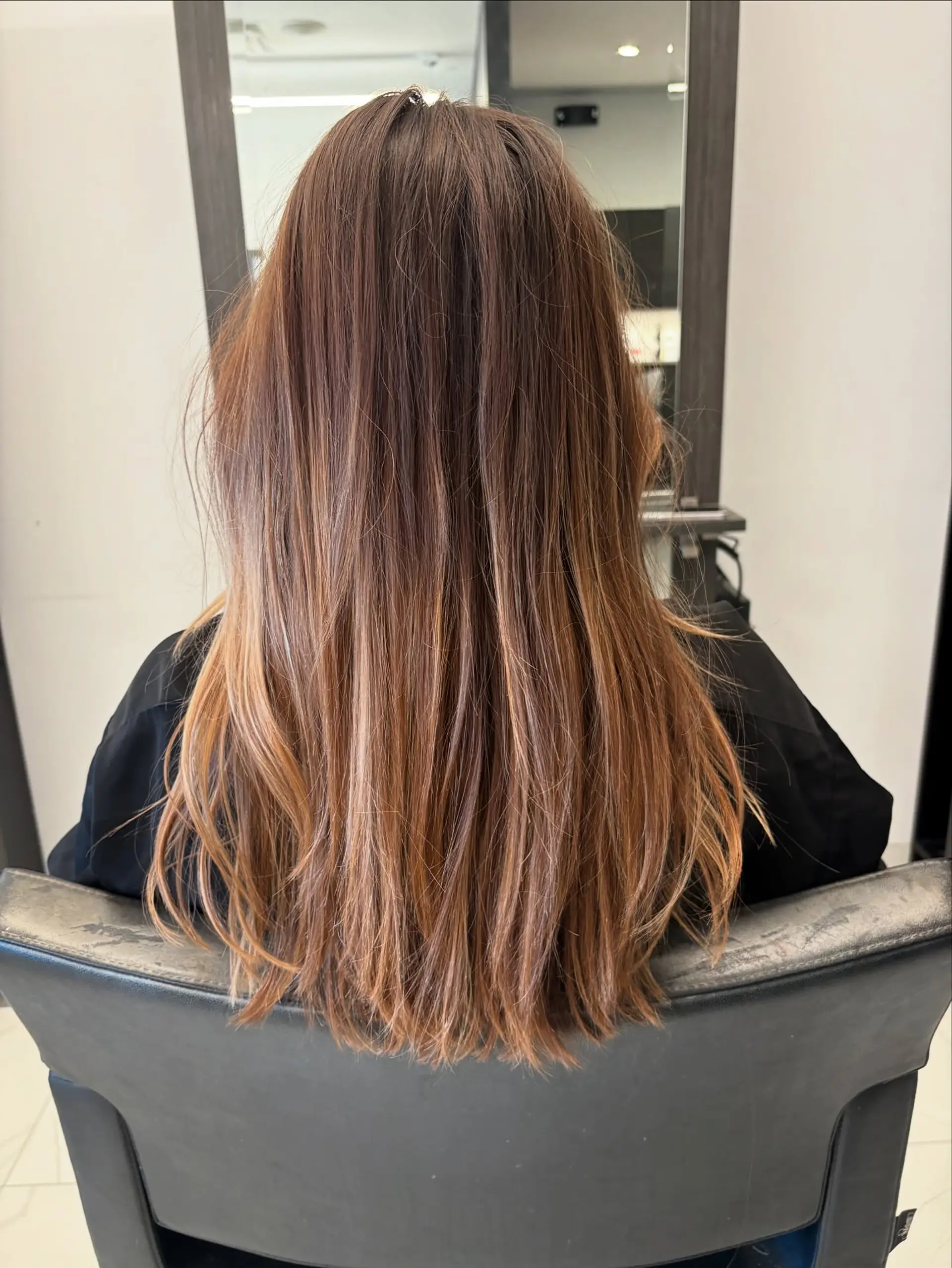 Long straight to subtly textured hair featuring a warm caramel and honey-toned balayage over a soft brown base. 1