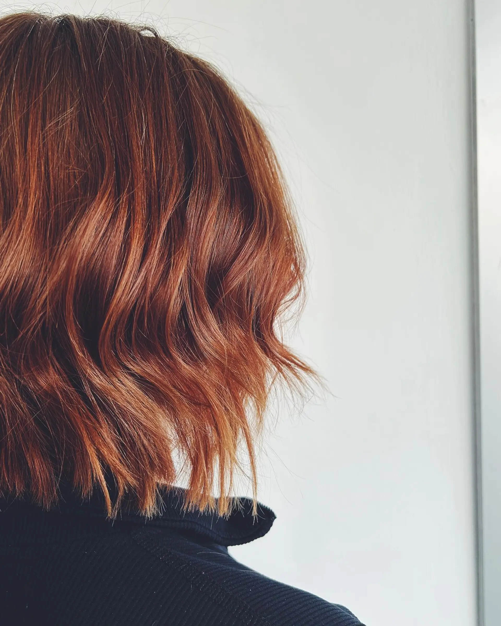 A textured chin-to-neck length bob featuring soft waves and warm copper-red color. 1