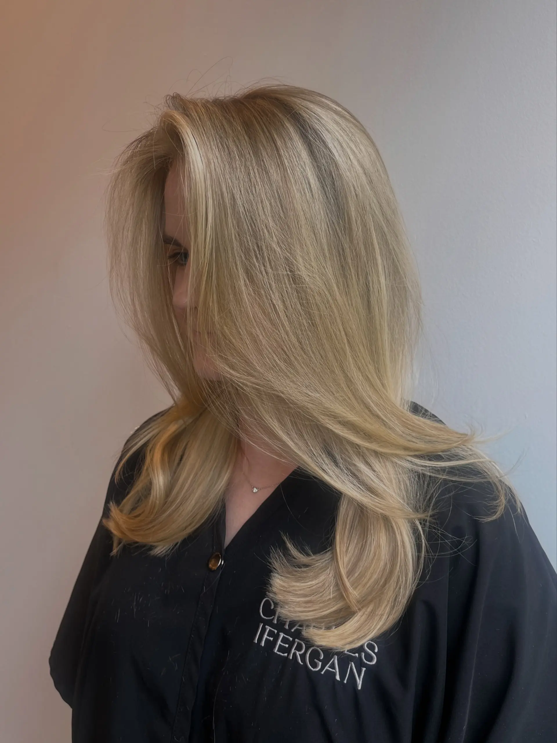 Long creamy blonde hair cut in face-framing layers and styled with a smooth, voluminous blowout featuring soft flicked ends. 1