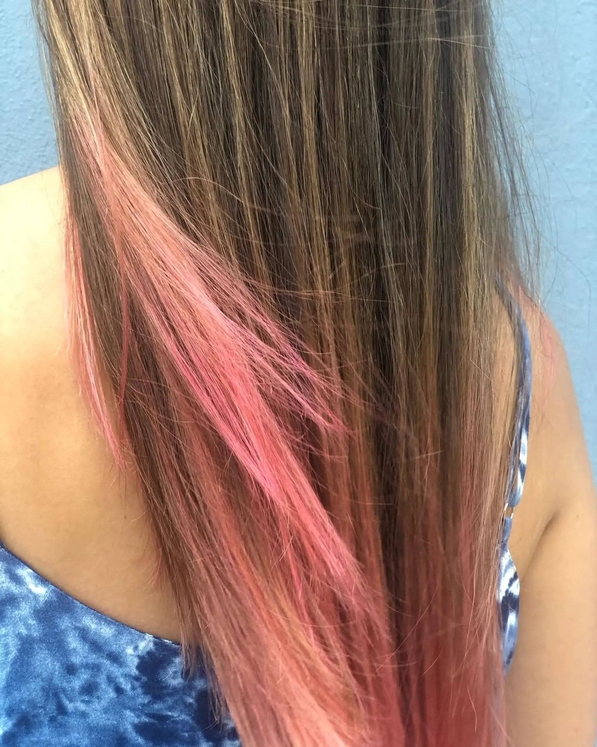 Long, straight brown hair with an ombre effect transitioning to pink, featuring layers that enhance movement.