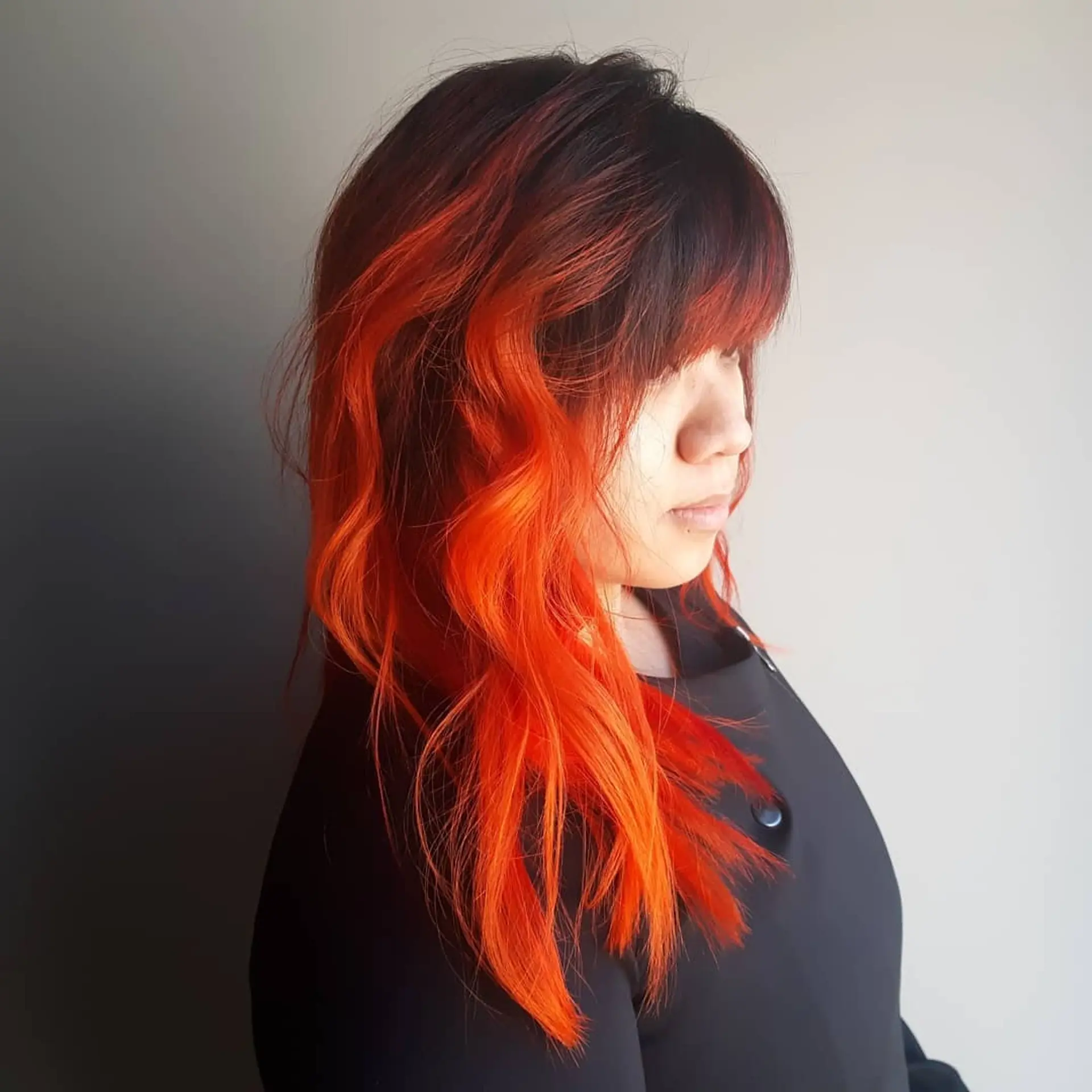 A striking medium-length wavy hairstyle featuring a bold black to orange ombre and full bangs. 1