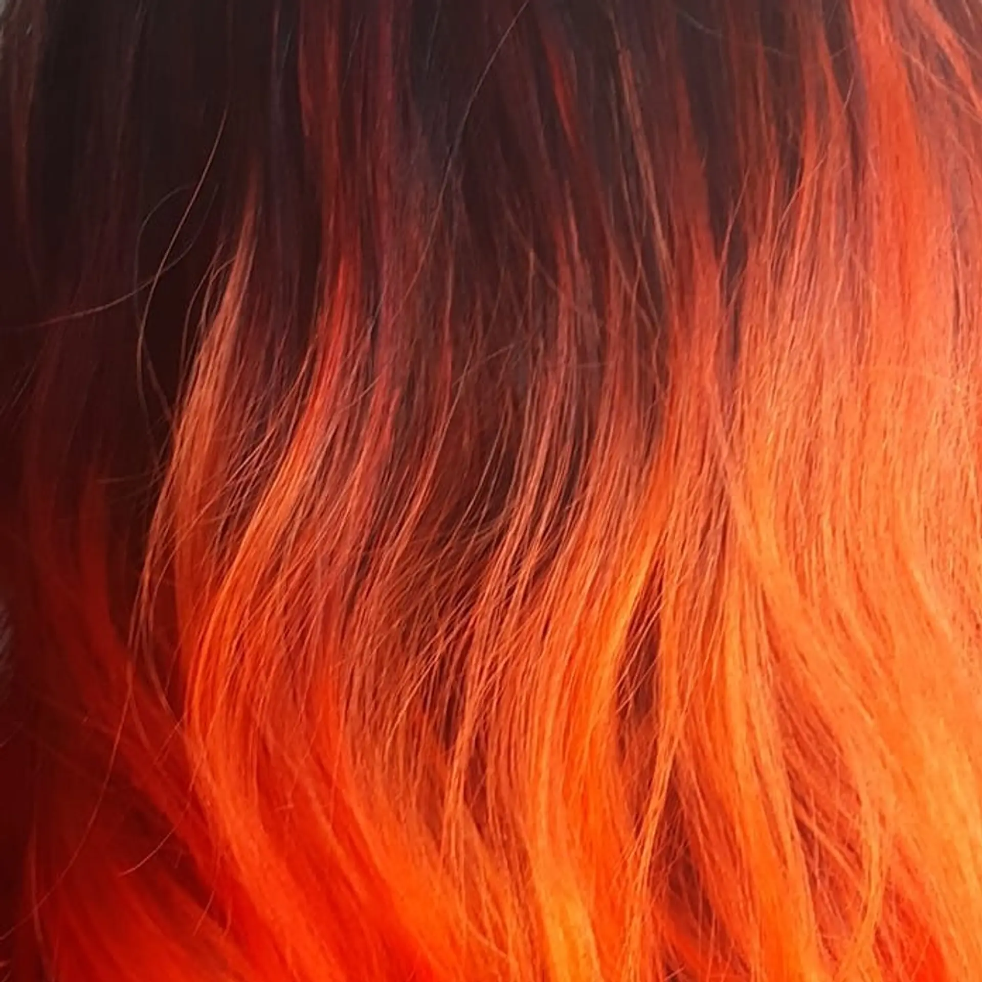 A striking medium-length wavy hairstyle featuring a bold black to orange ombre and full bangs. 2