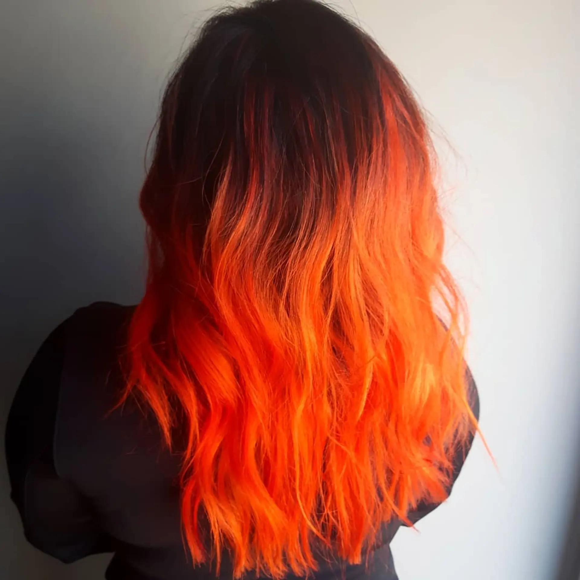A striking medium-length wavy hairstyle featuring a bold black to orange ombre and full bangs. 3