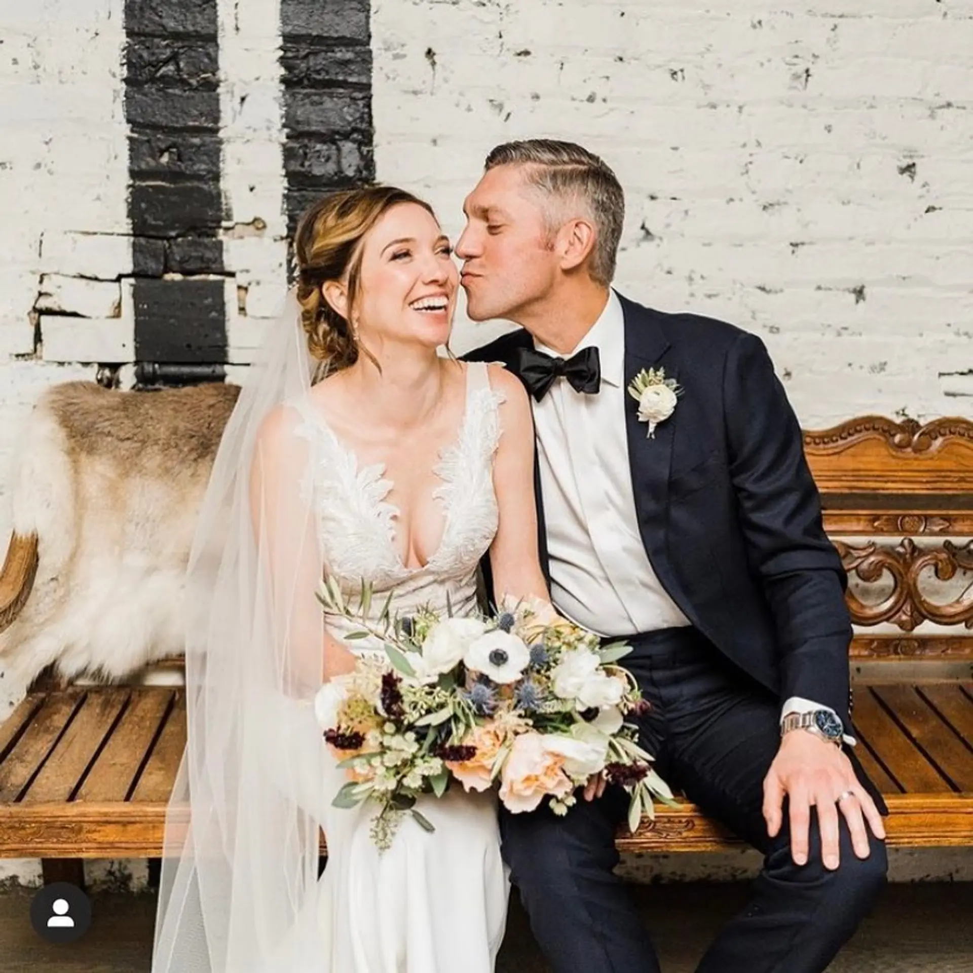 A soft, romantic bridal updo styled at the nape of the neck with subtle face-framing waves and an attached veil. 1