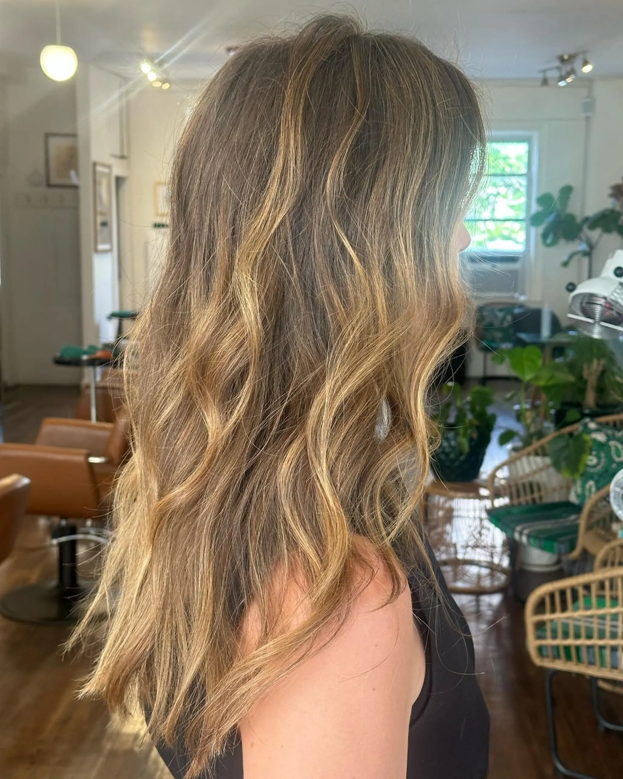Long, wavy hair with natural blonde and light brown highlights, featuring a layered cut that enhances texture and movement.