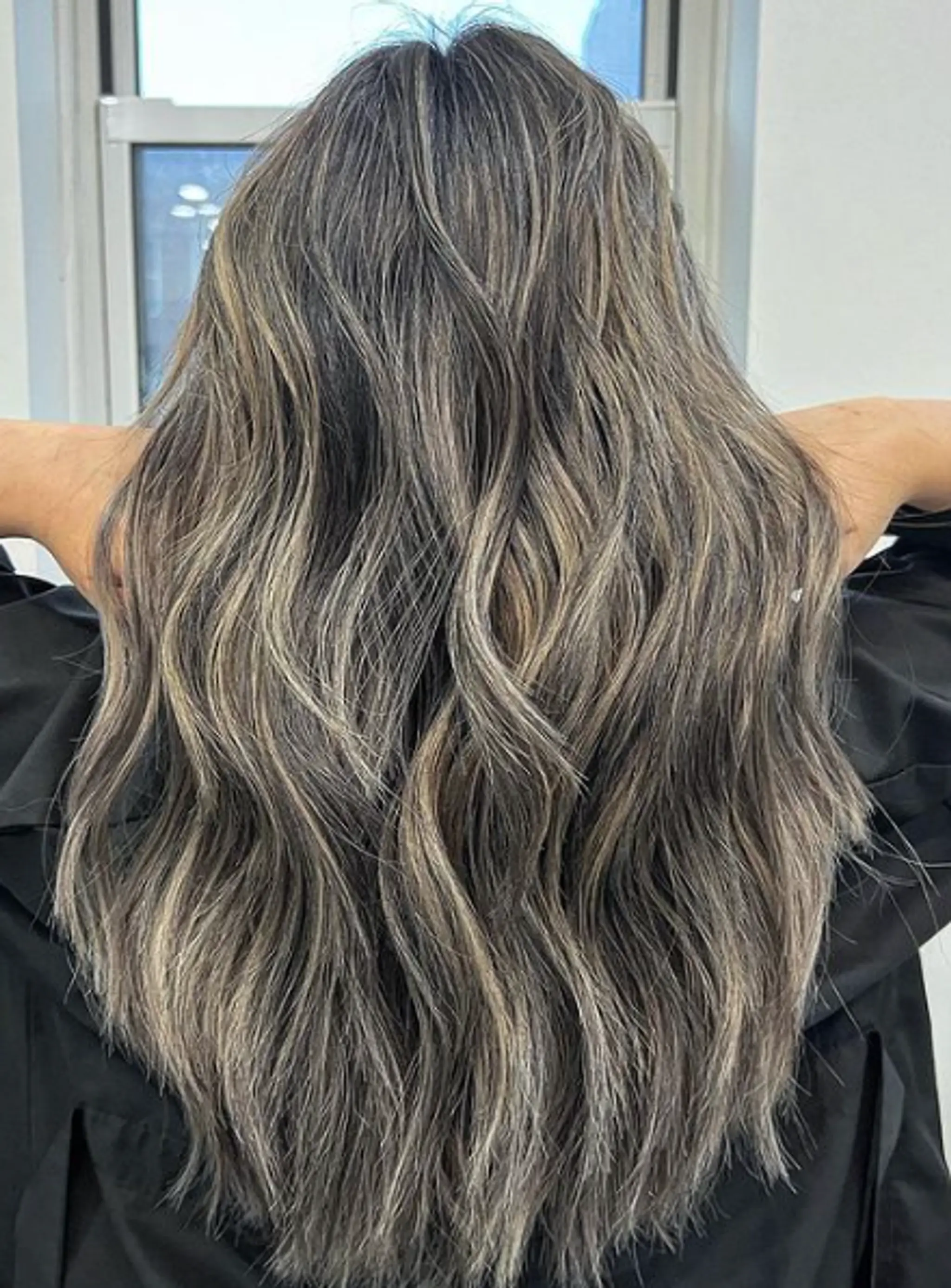 Long, wavy hair with ash blonde and silver tones, featuring dark roots and a natural, flowing wave pattern.