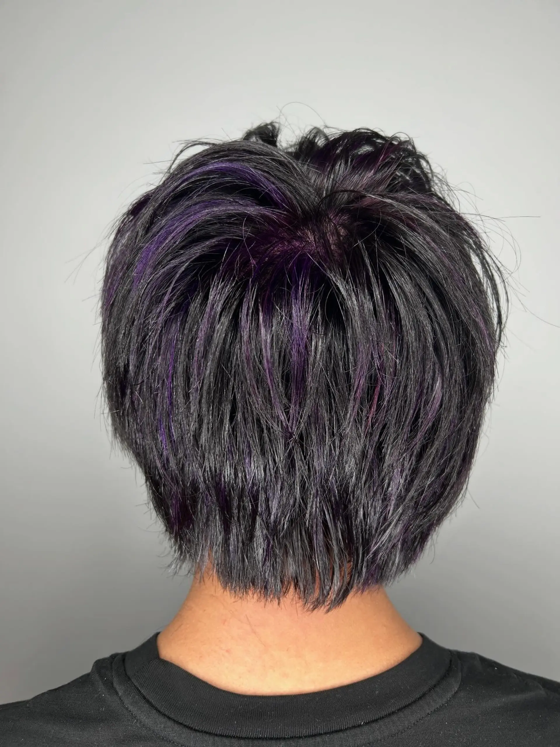 A textured short pixie cut featuring piecey layers and subtle violet-purple highlights throughout dark hair. 1
