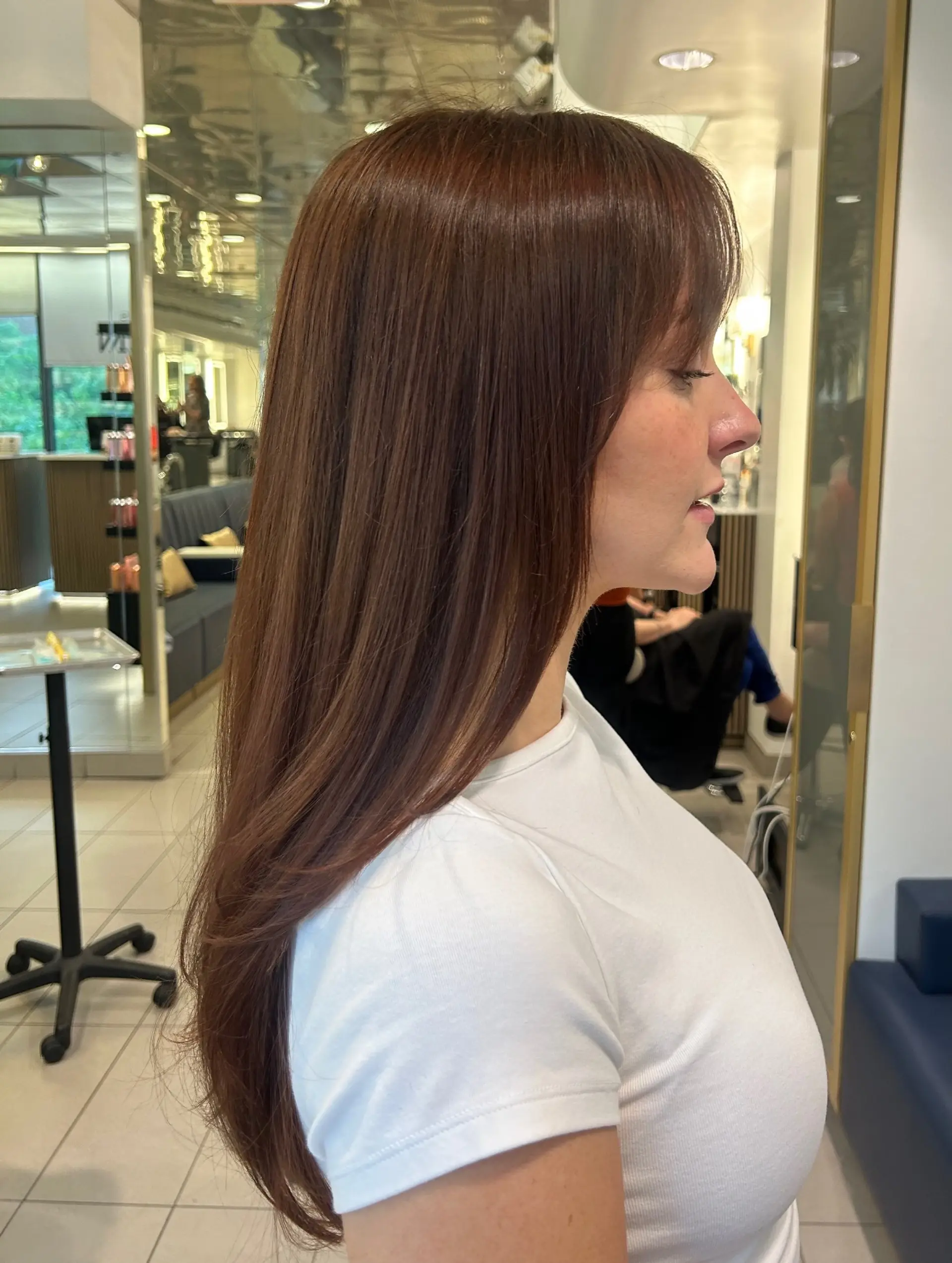 Long, sleek auburn hair styled straight with soft, textured bangs and slightly curved ends. 1