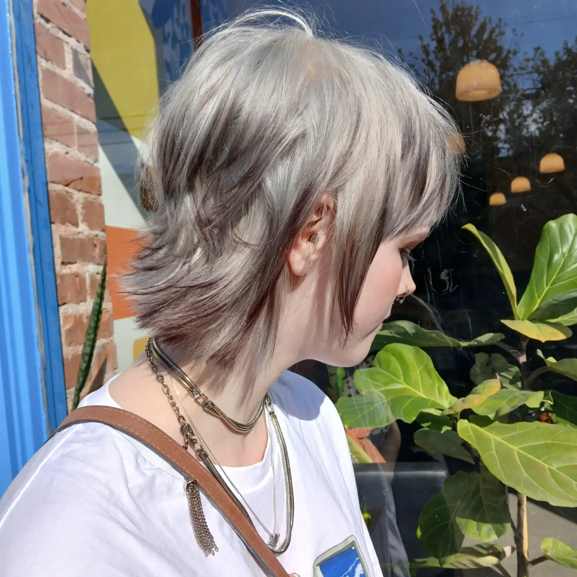 A textured platinum blonde shaggy mullet haircut featuring contrasting dark brown peekaboo lowlights. 1