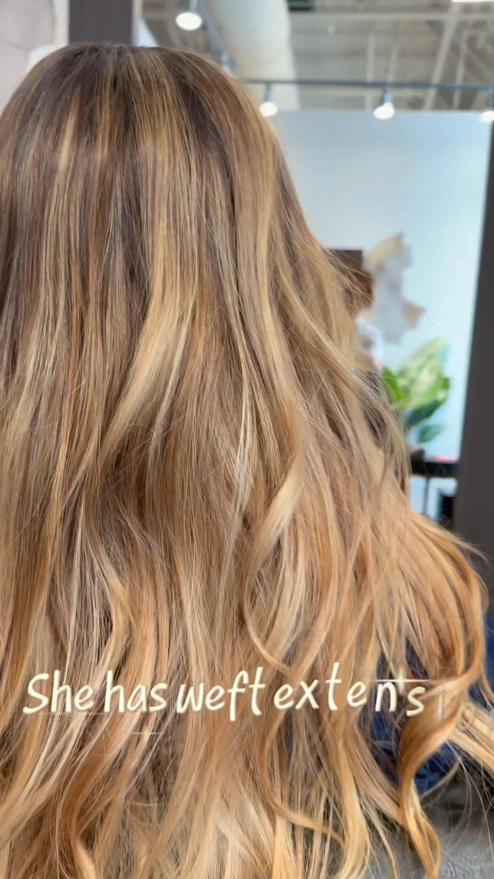 Long, dimensional warm blonde hair styled in soft, loose waves featuring blended weft extensions. 1
