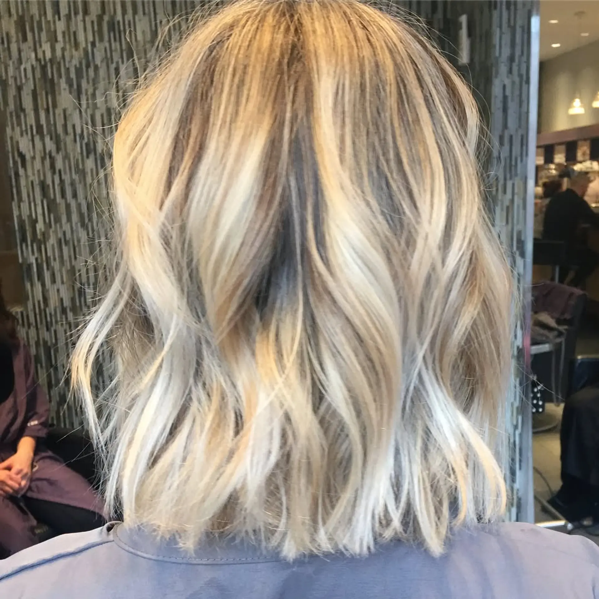 A shoulder-length textured lob featuring bright dimensional blonde highlights and effortless, relaxed waves. 1