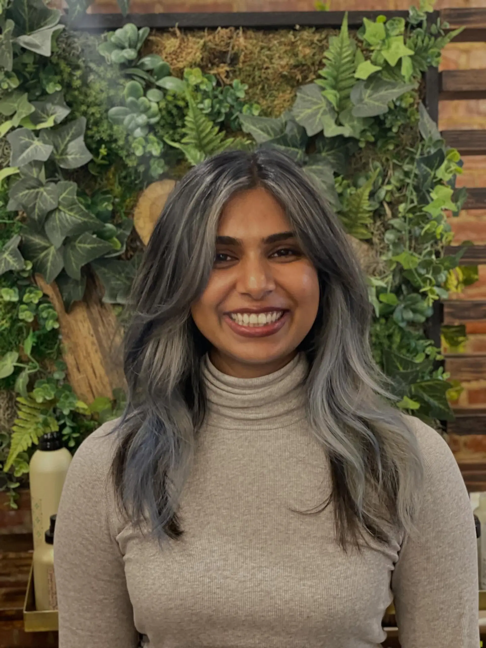 Medium-length wavy layered cut with soft curtain bangs, featuring cool-toned smokey silver highlights over a dark base. 1