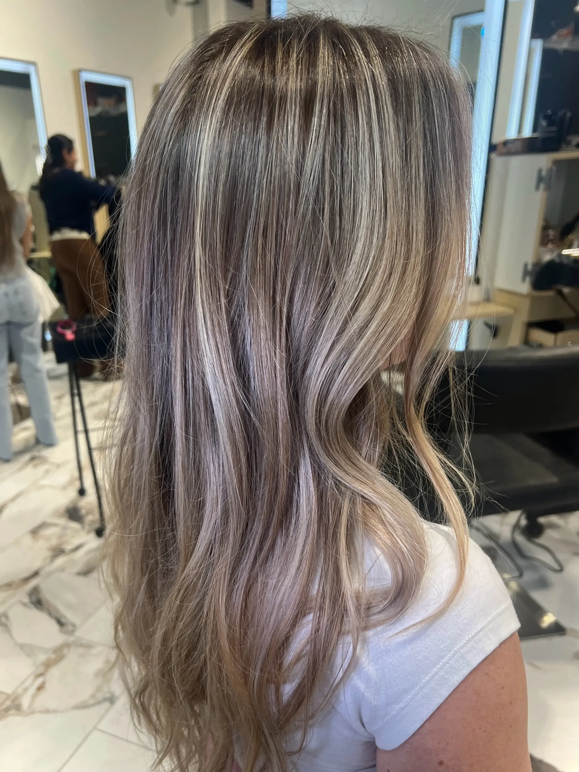 Long hair featuring highly dimensional, fine blonde highlights seamlessly blended over a rooted base with soft waves. 1
