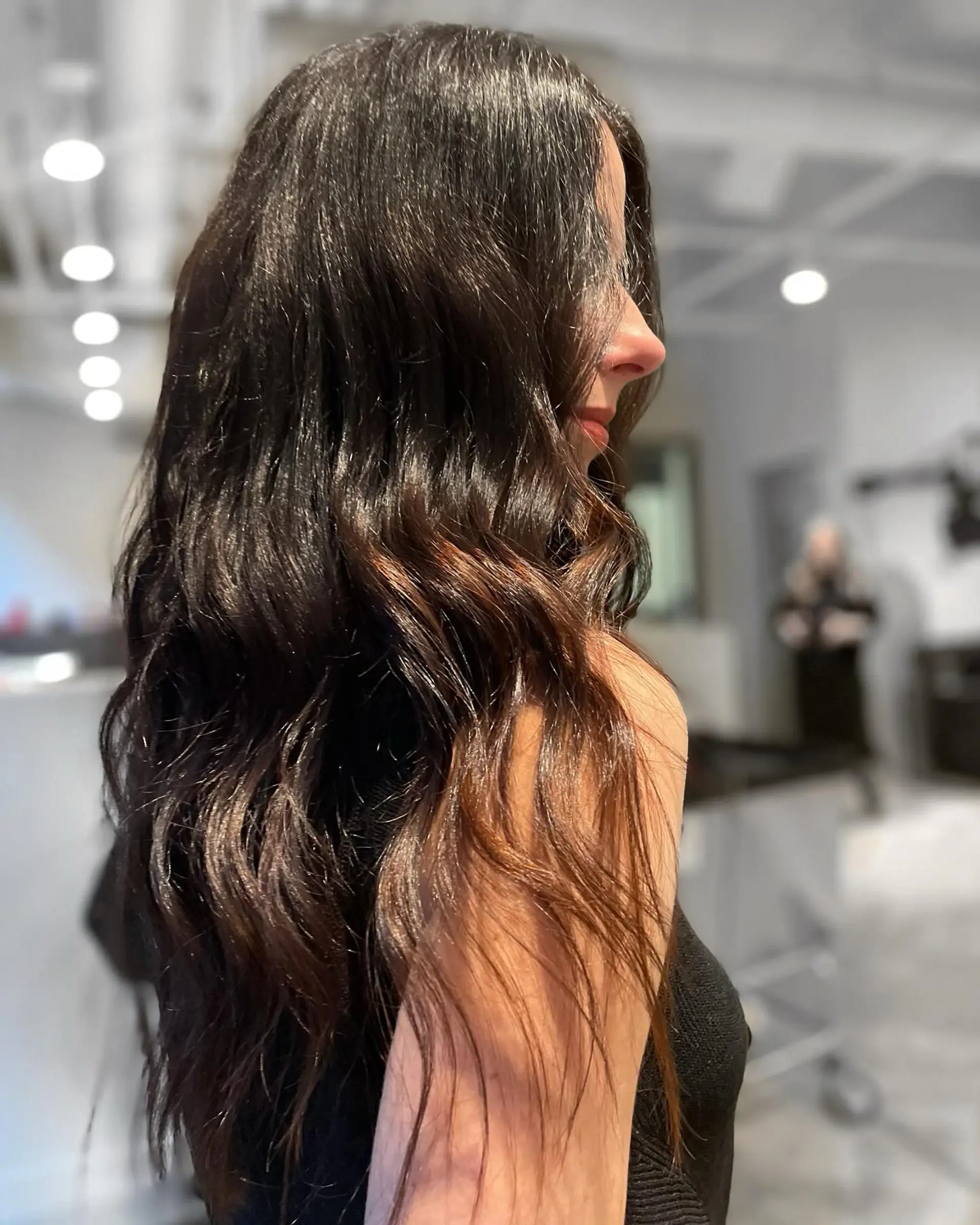 Long, glossy brunette hair styled with soft, loose waves featuring subtle dimensional warm tones. 1