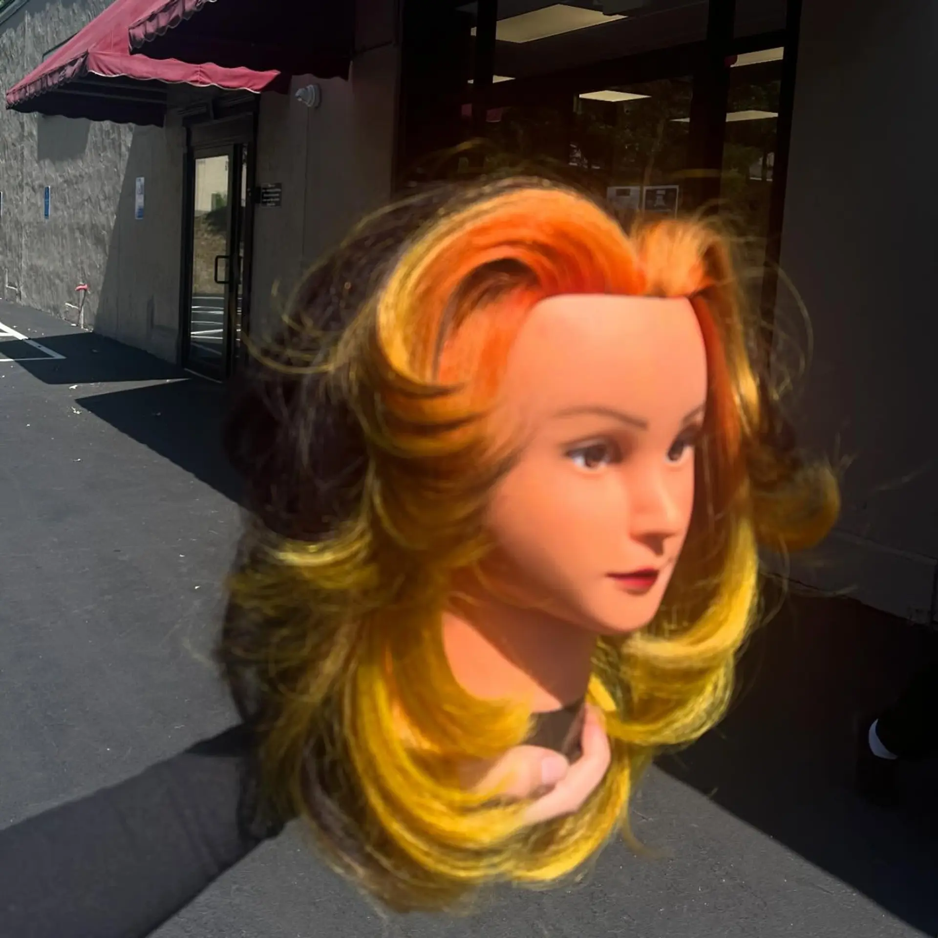 A mid-length layered cut styled with voluminous face-framing flips, featuring a dramatic sunset-inspired halo color melt blending bright orange, chartreuse yellow, and dark brown. 1