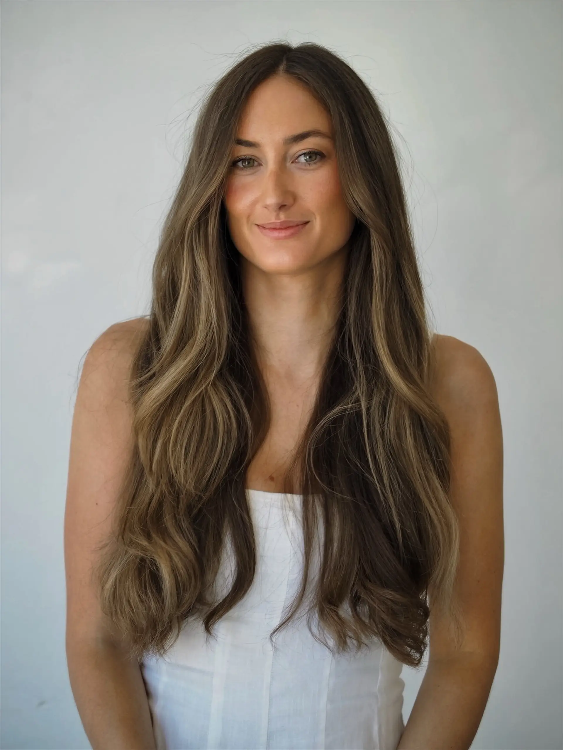 Long ash brunette hair with dimensional soft blonde highlights, styled in loose, natural waves with a center part. 1