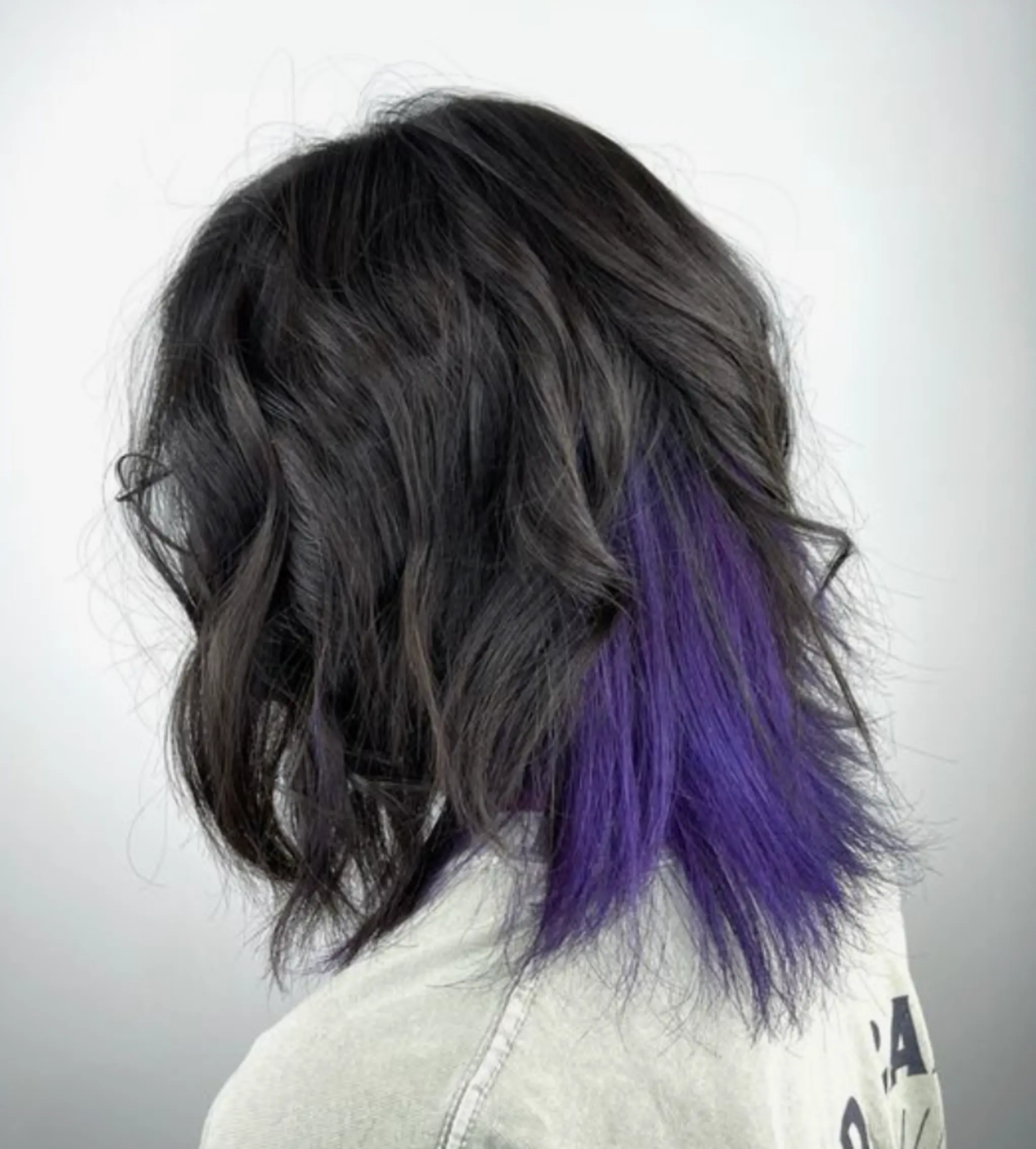 Medium-length, black hair with loose waves and a vibrant purple underdye.