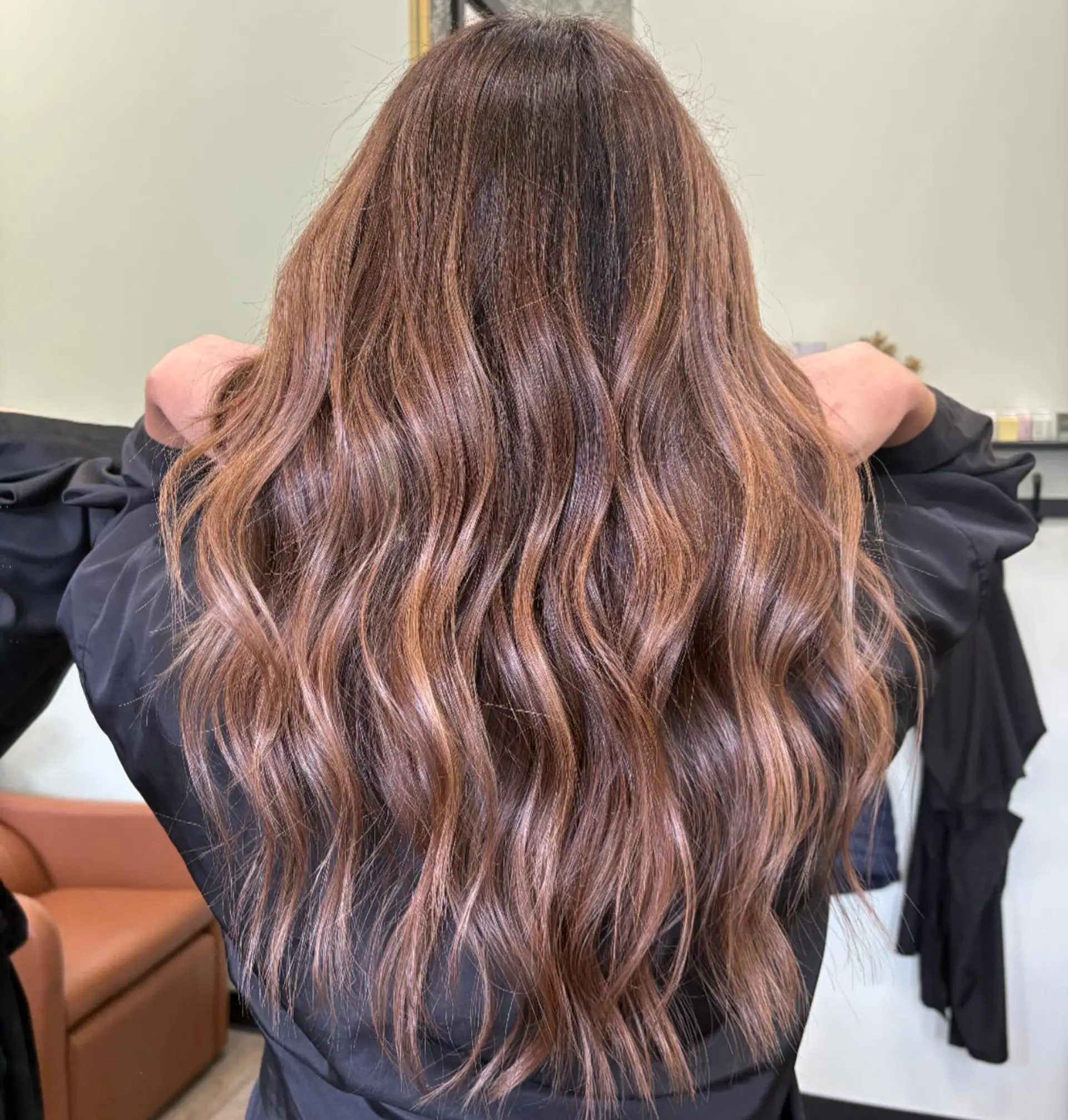 Long, dimensional warm brunette hair with subtle caramel highlights styled in soft waves. 1