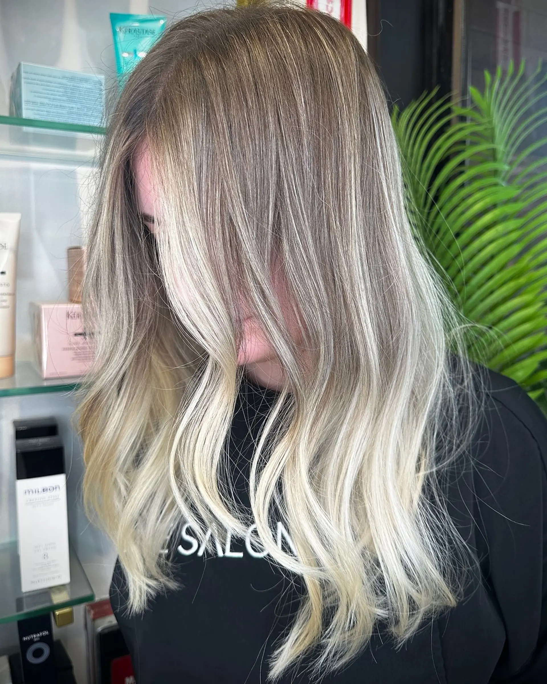 Long, wavy hair with an ash blonde to platinum blonde ombre. The style is achieved using balayage techniques for a gradual lightening effect, with a middle part and soft, flowing waves. 1
