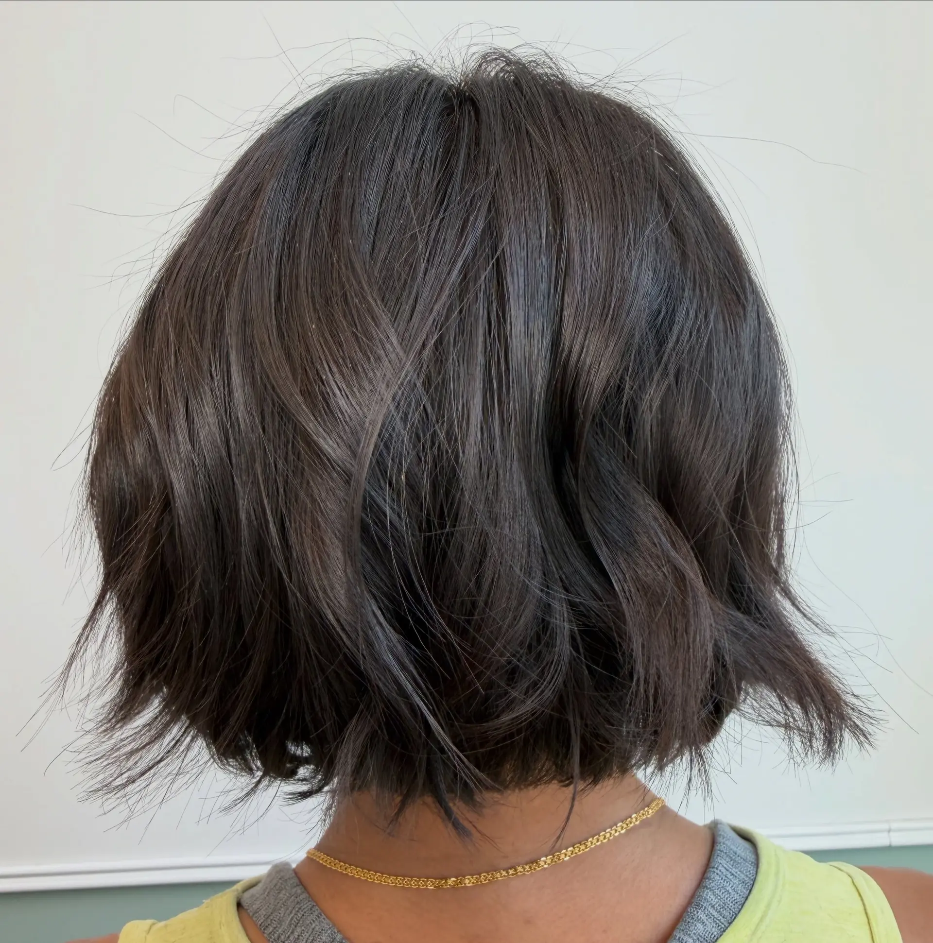 A chin-length textured bob cut in a rich dark brunette tone, styled with effortless, tousled waves. 1