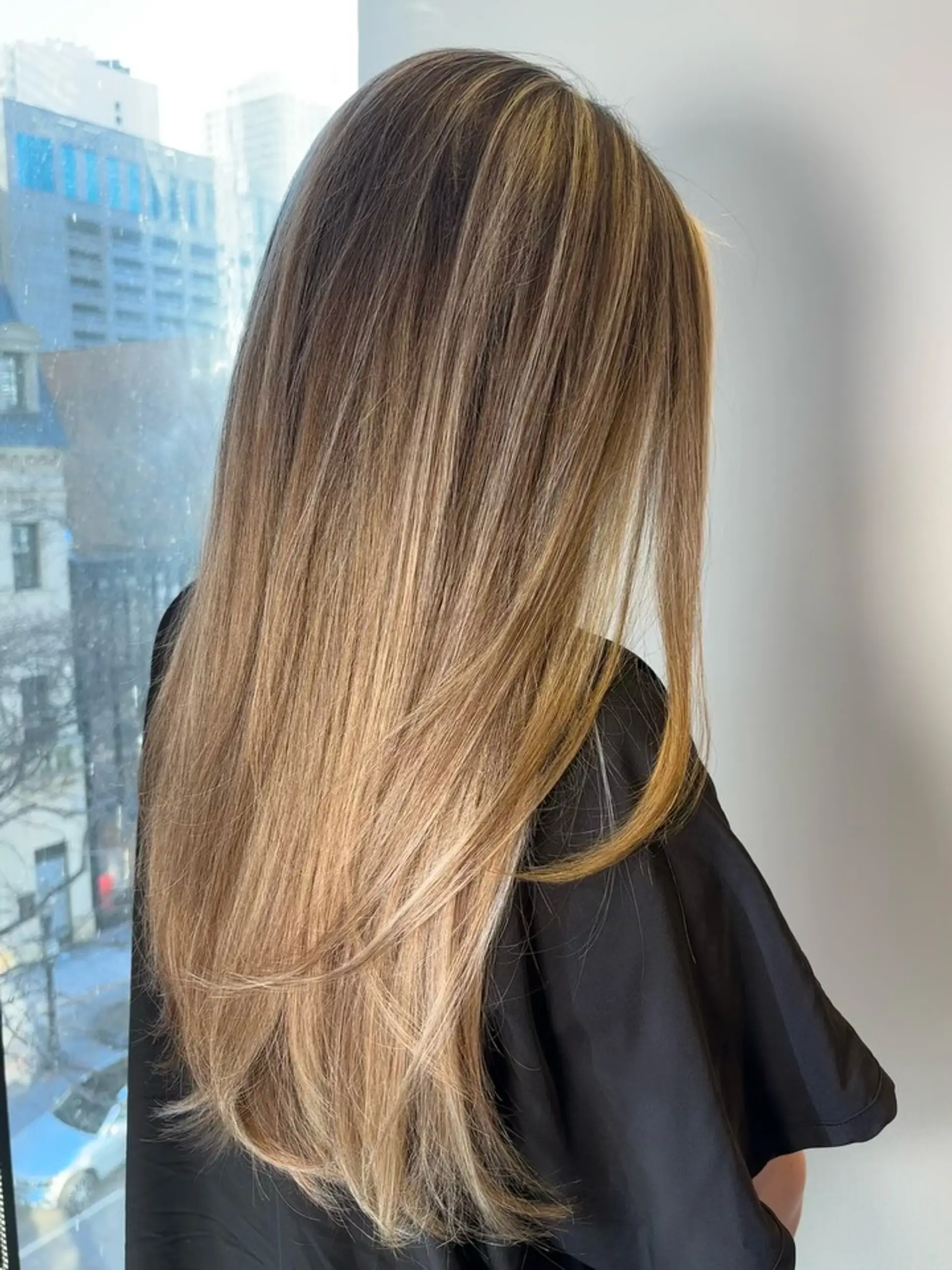 Long, sleek straight hair featuring dimensional caramel and honey blonde balayage over a warm light brown base with soft face-framing layers. 1