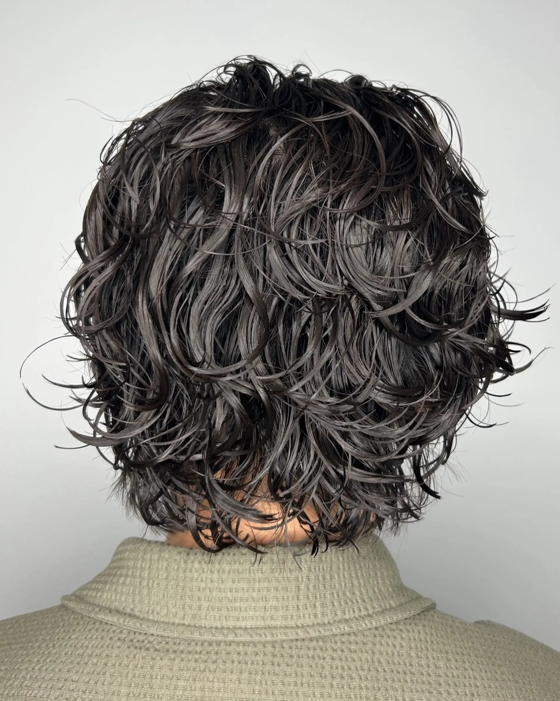 A short, layered haircut styled with defined, textured waves and curls with a wet-look finish. 1
