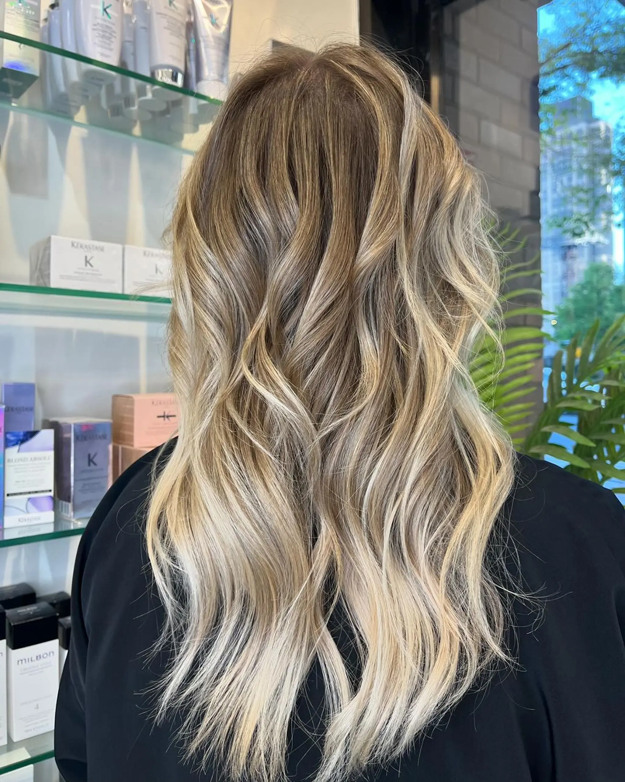 A long wavy hairstyle with golden blonde and honey tones, featuring dimensional highlights and layered cut for added movement and volume.
