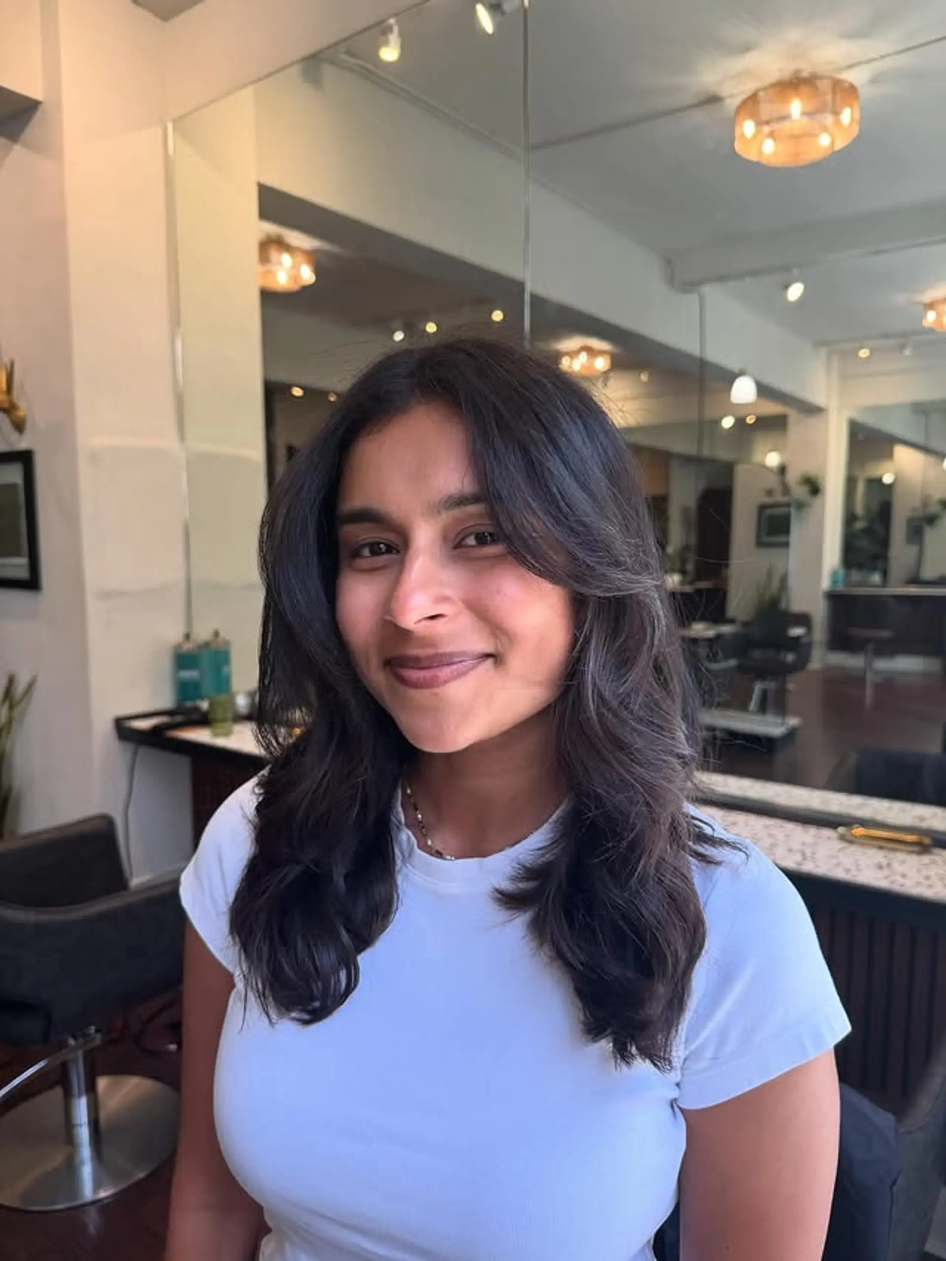 A medium-length layered hairstyle with soft waves and face-framing curtain bangs. 1