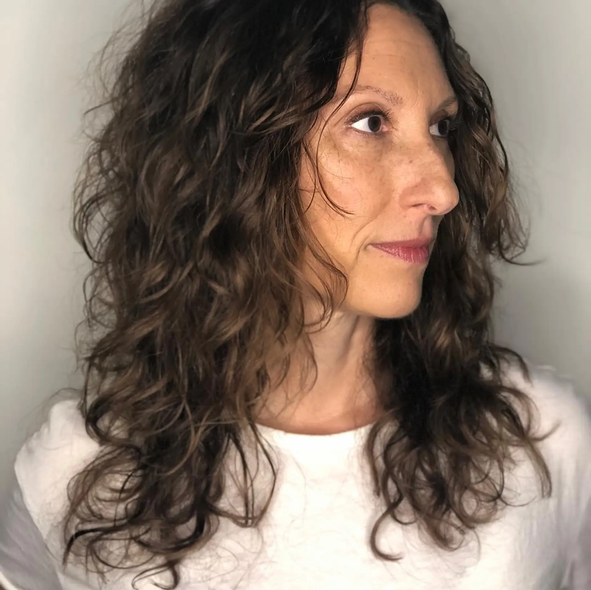 A medium-length layered haircut designed to enhance natural curls and texture with face-framing layers and crown volume. 1