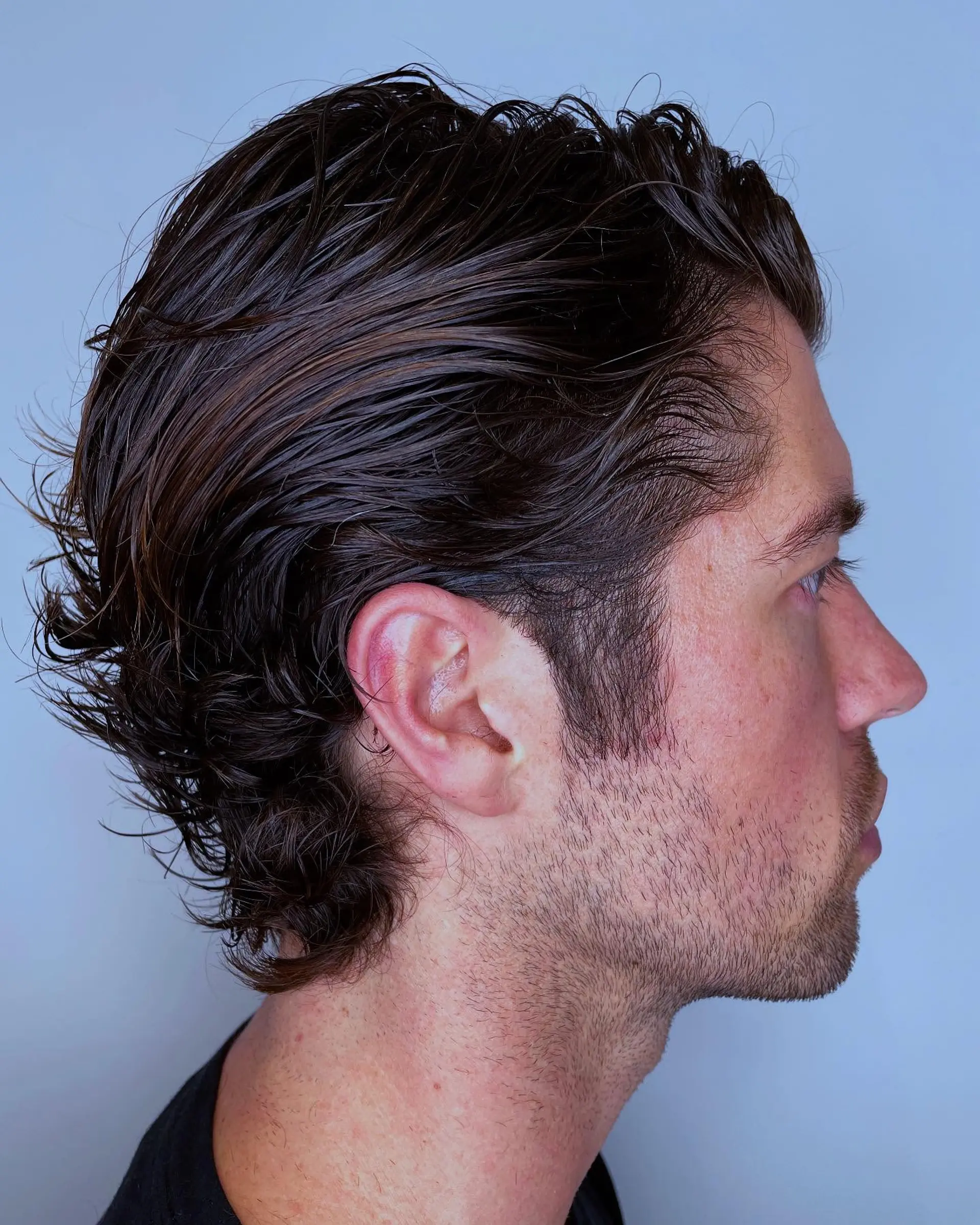 A textured, slicked-back medium-to-short flow haircut with natural waves swept behind the ear and neck. 1