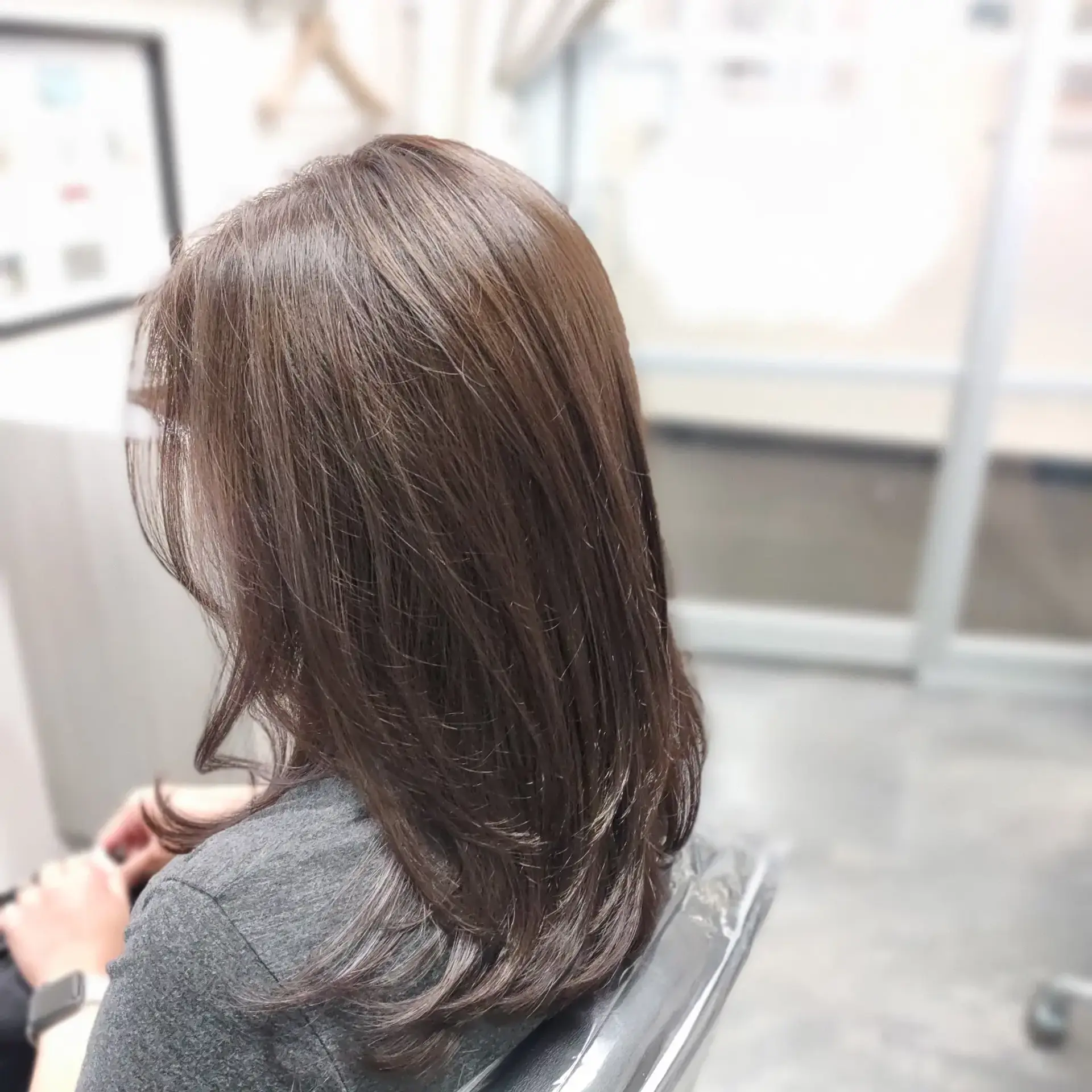 Medium-length layered haircut in a glossy ash brown tone, styled with subtle movement and soft flips at the ends. 1