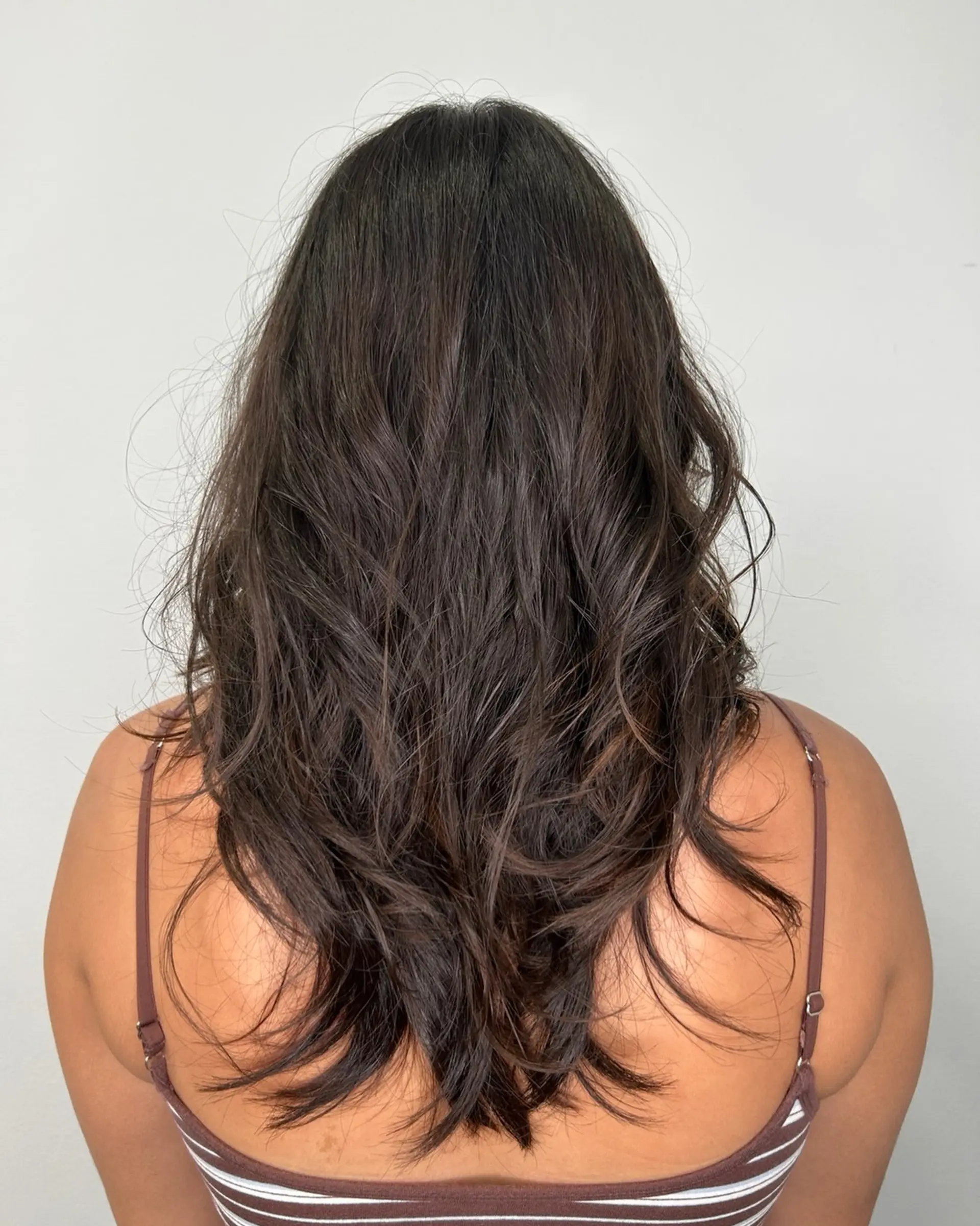 Long dark brown hair cut in cascading layers with soft, tousled body waves. 1