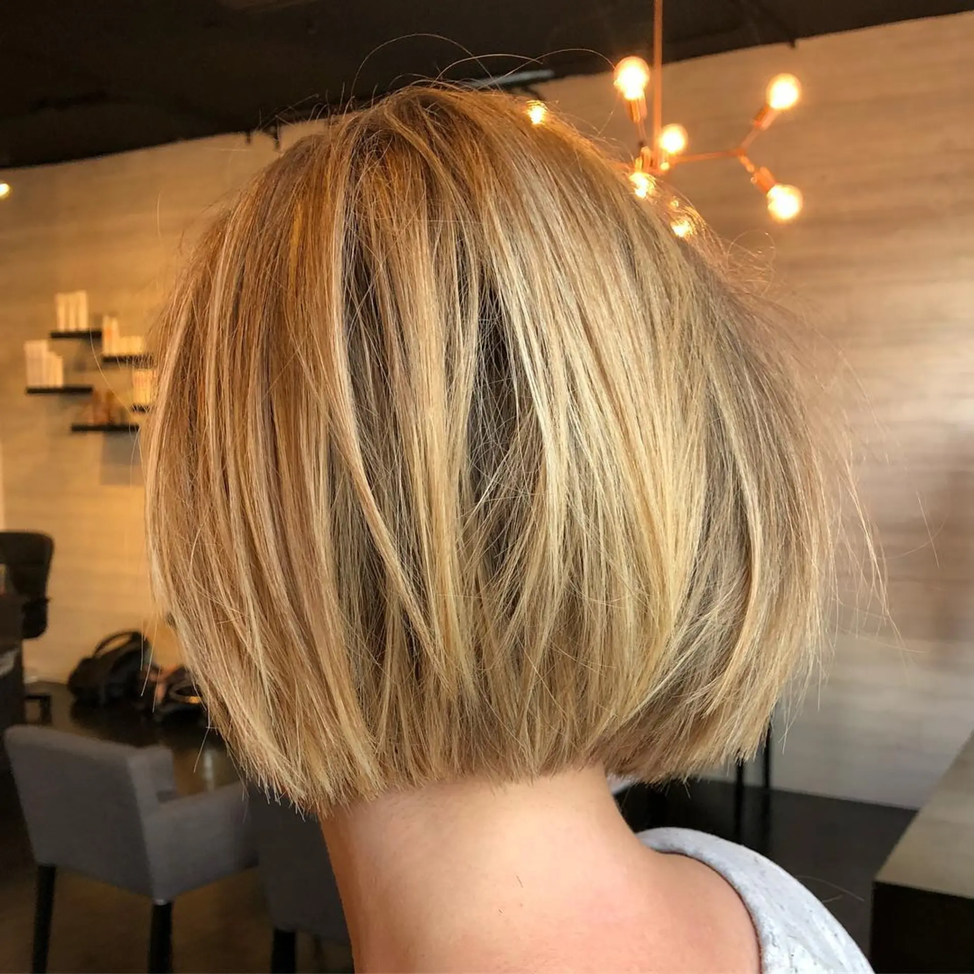 A short textured blonde bob featuring multi-tonal dimensional highlights and an undercut nape. 1