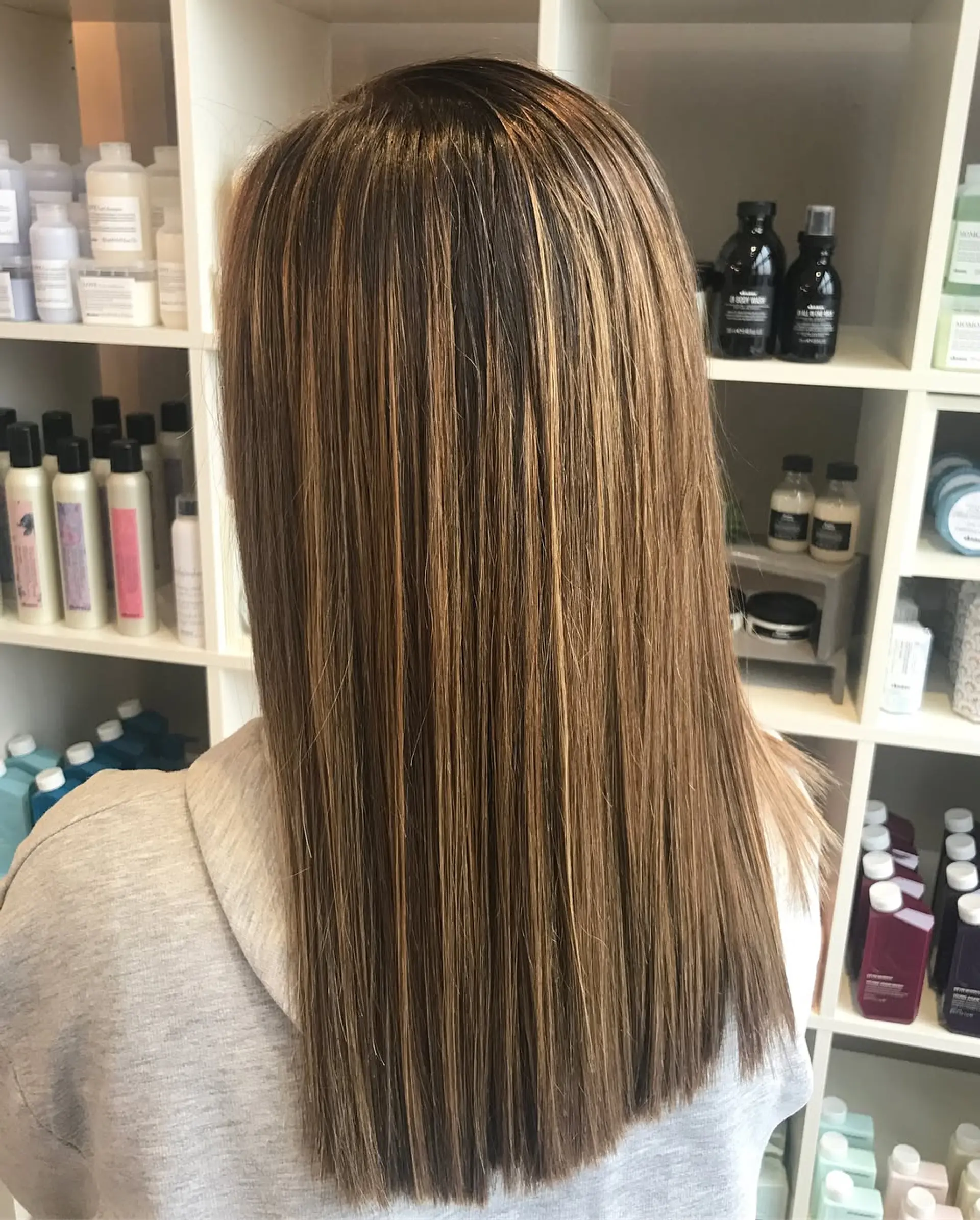 Long, sleek straight hair featuring a dimensional caramel balayage blended over a rich brown base. 1