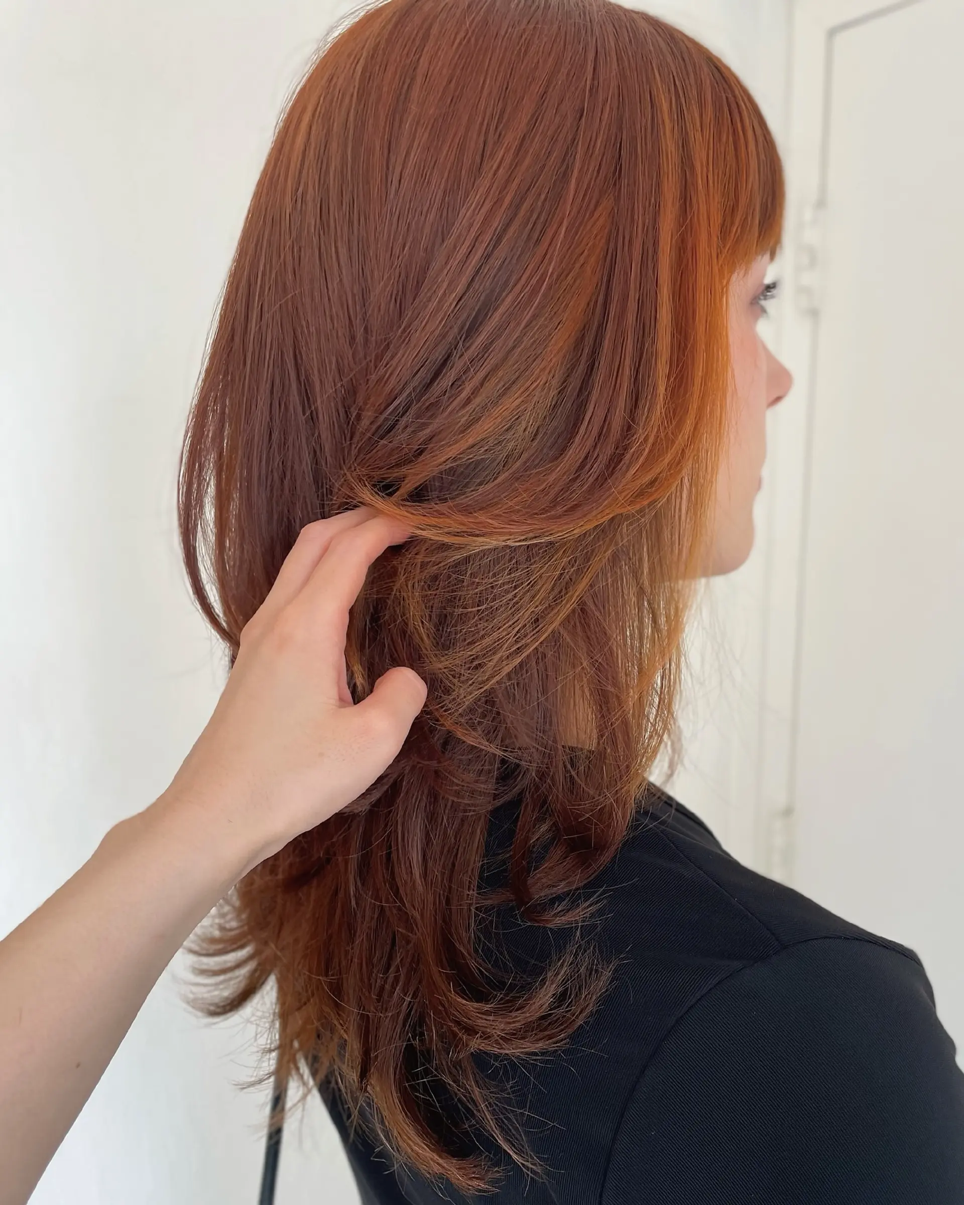 A textured modern wolf cut with face-framing layers, bangs, and soft flicked ends in a rich auburn copper tone. 1