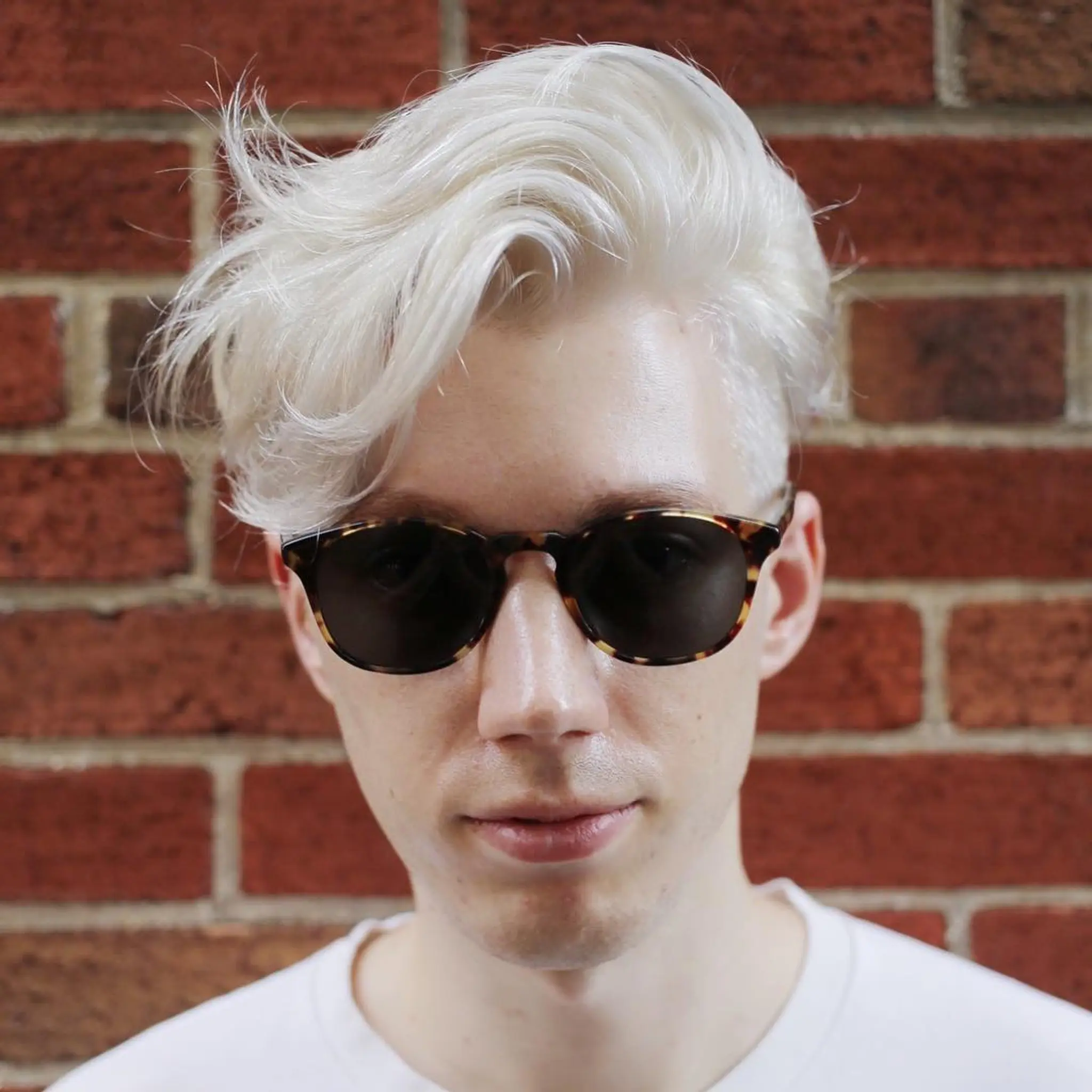 A modern and striking hairstyle characterized by platinum blonde medium-length wavy hair. It is styled with volume and movement, swept back and to the side, creating a dynamic and stylish effect. The front is longer and slightly tousled, giving a relaxed yet polished finish.